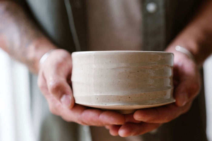 Close-up of hands gently holding a handmade ceramic matcha bowl (chawan) with a natural matte glaze — crafted by IKKAI Ceramics.