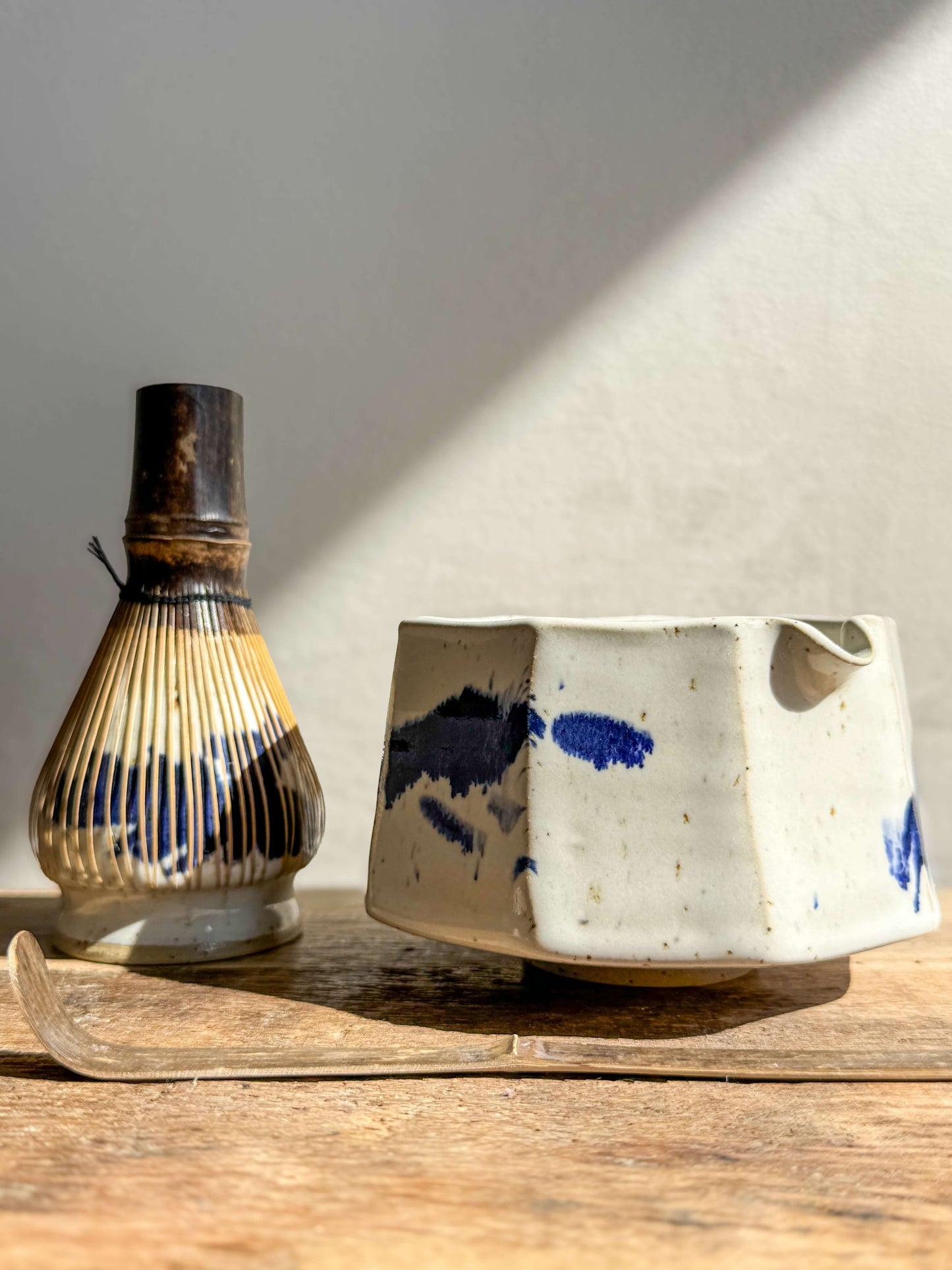 Faceted matcha bowl with spout in cobalt blue and glossy white glaze, featuring unique facets for a modern look, alongside a bamboo whisk.