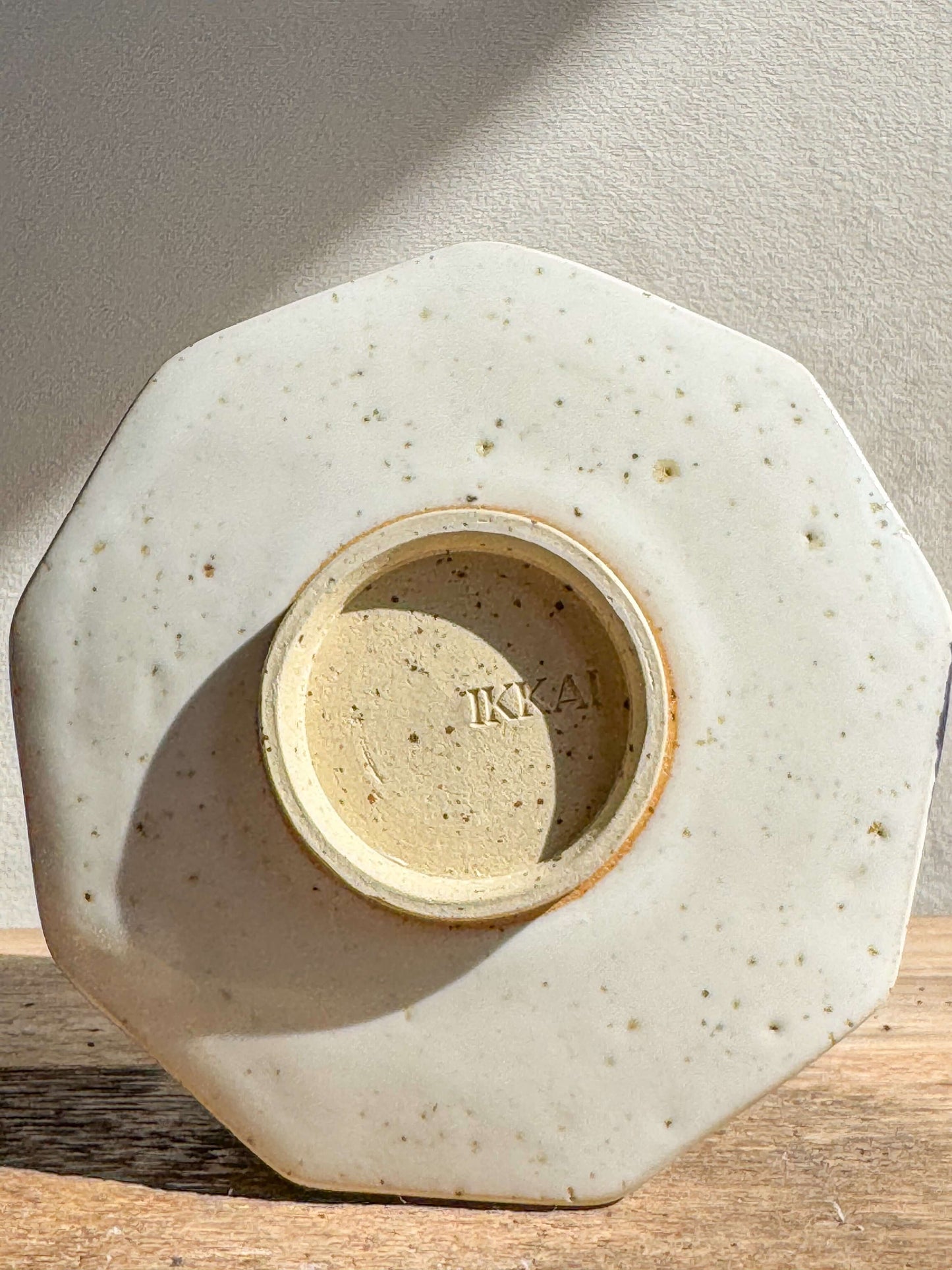 Bottom view of a faceted ceramic bowl with a white glaze, revealing textured details and a maker's mark on a wooden surface.