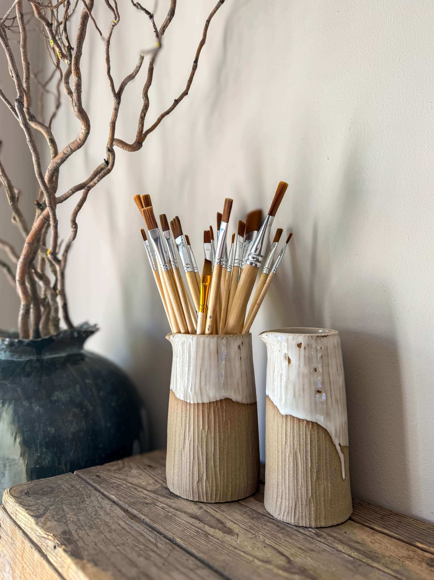 Sculptural medium vase from Yuki Series with hand-carved texture and glossy white glaze, displayed with paintbrushes on wooden shelf.