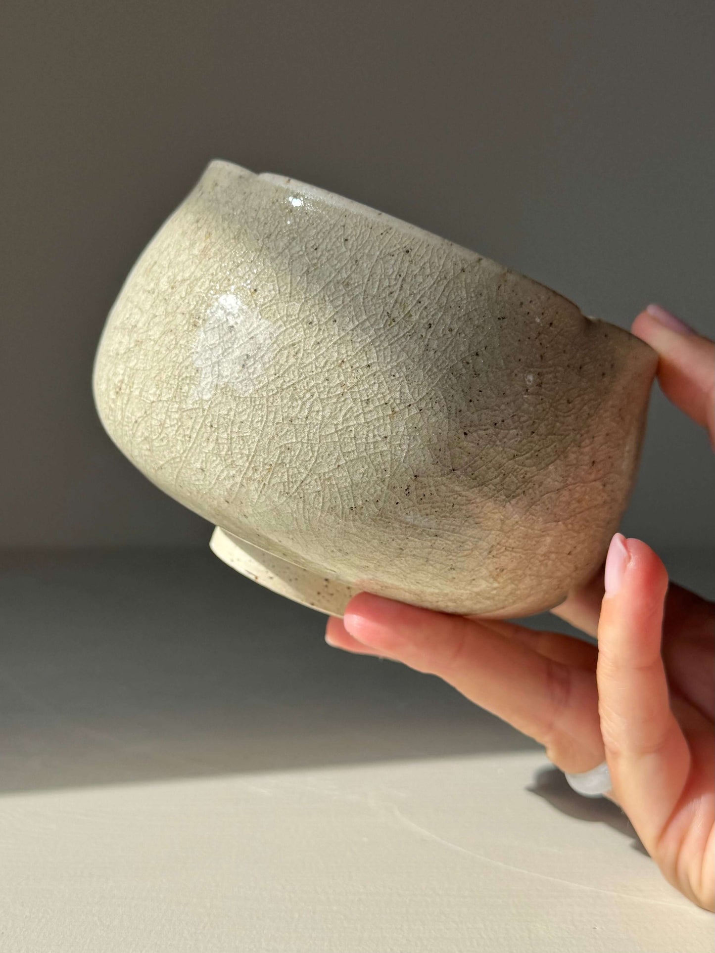 Handmade ceramic Matcha Bowl - Kannyū #01 with soft flower-like shape and clear crackle glaze, held in hand.