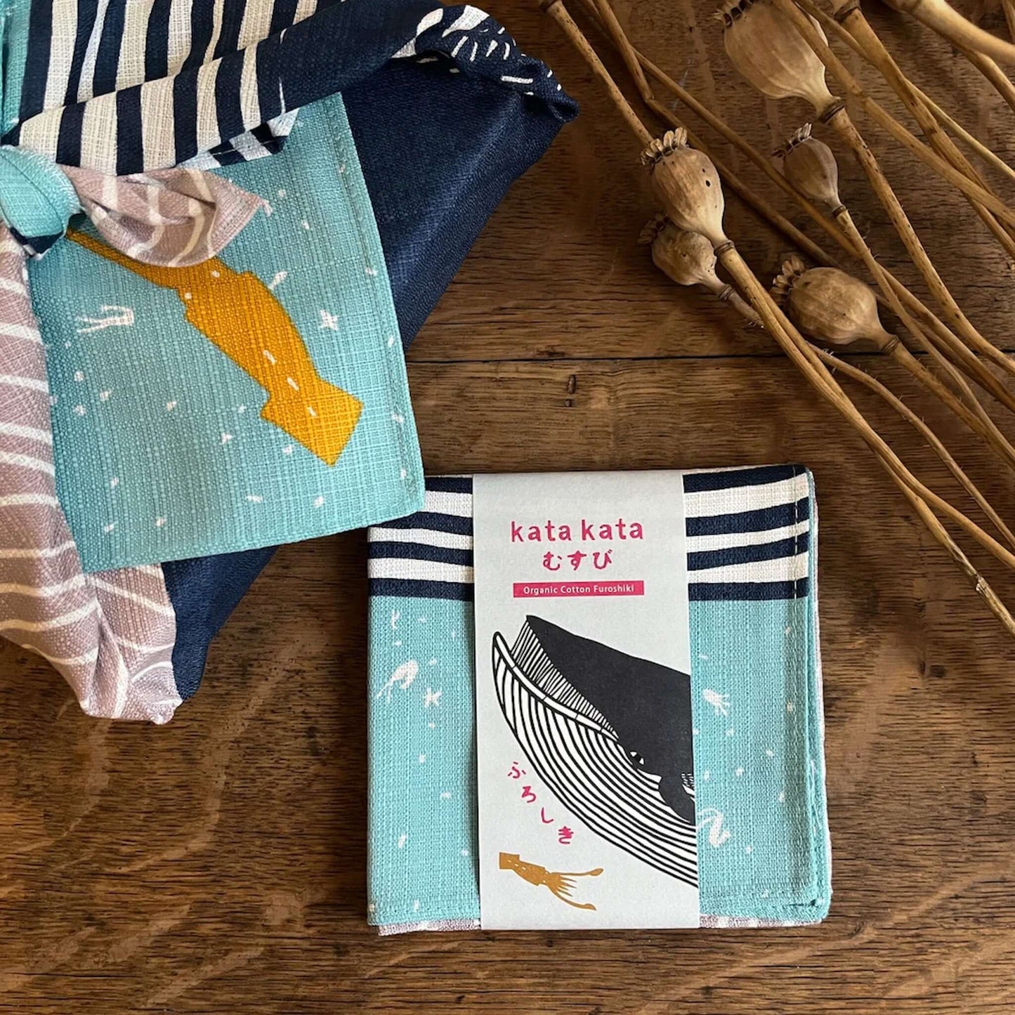 Small Furoshiki kata kata musubi organic cotton Blue Whale with patterned fabric and a label on a wooden surface.