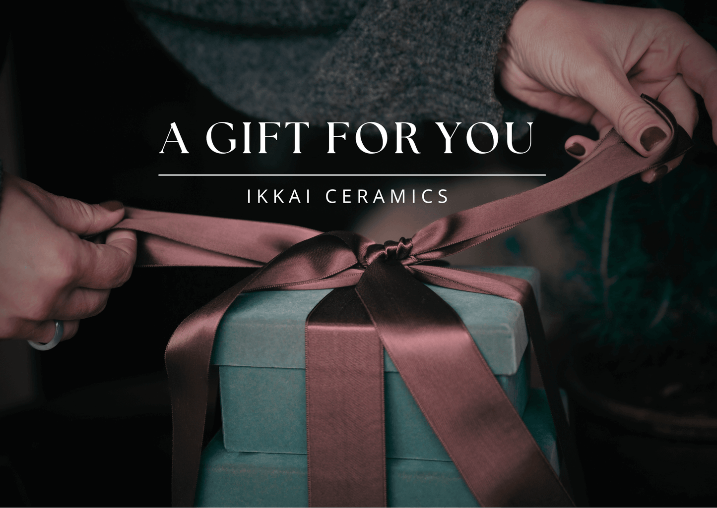 Hands tying bow on gift box with IKKAI Ceramics Gift Card label, perfect choice for sharing handmade ceramics joy.