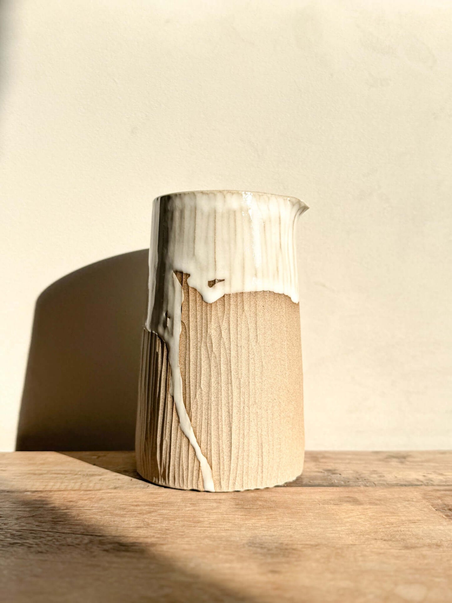 Medium vase jug from Yuki Series #01 with hand-carved lines, glossy white glaze on top, and natural unglazed base, sunlit setting.