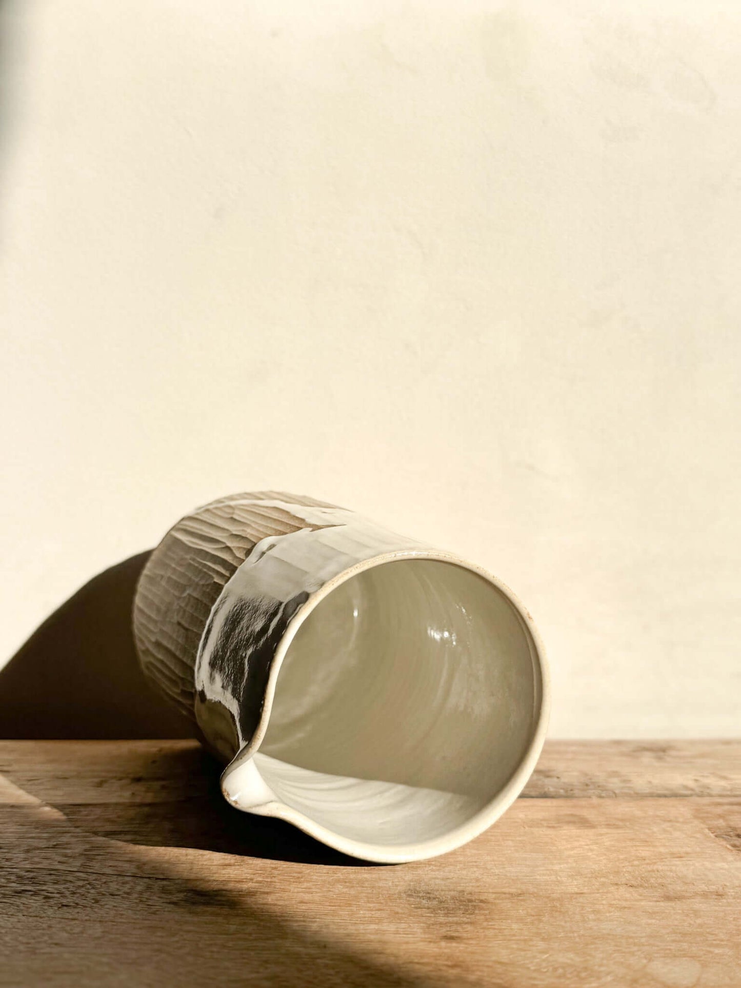 Medium Yuki Series vase with hand-carved lines and glossy white glaze, lying on its side on a wooden surface, showing soft textures.