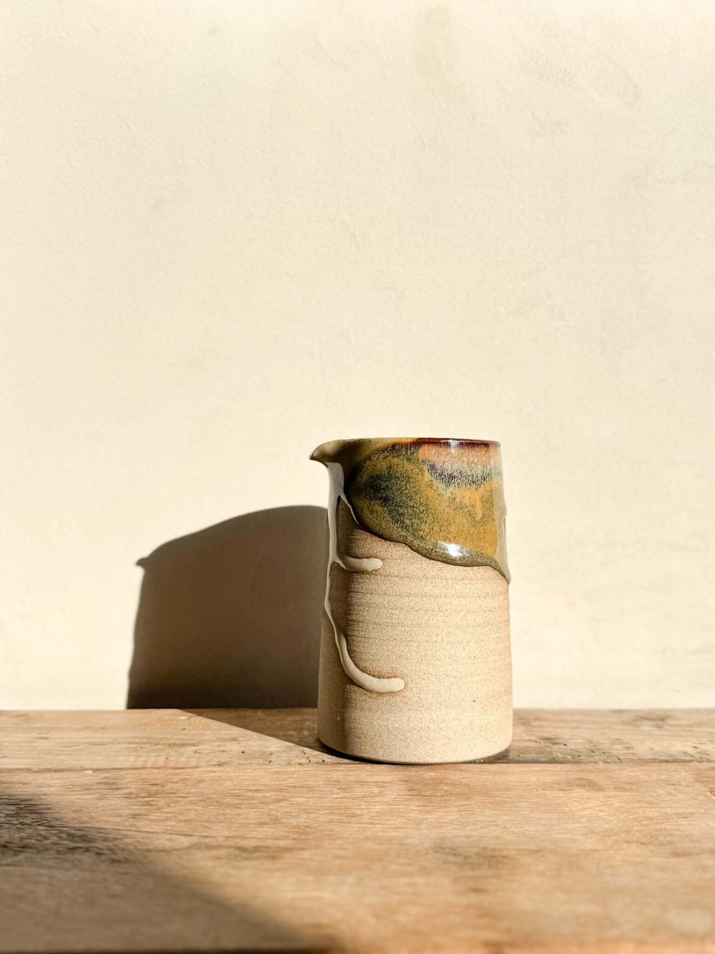 Tall sculptural vase jug from Inyo Series with raw texture and flowing glaze, suitable as vase or water jug, on wooden surface in sunlight.