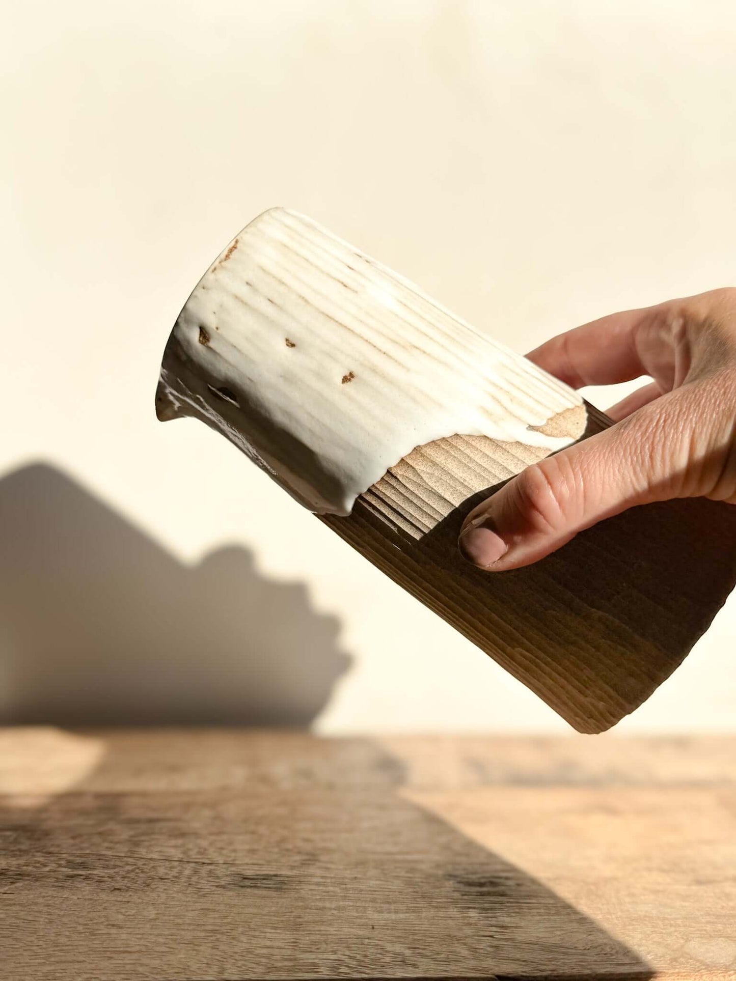 Hand holding a medium-sized Yuki Series vase with vertical lines, glossy white top, and raw unglazed base, resembling wood grain.