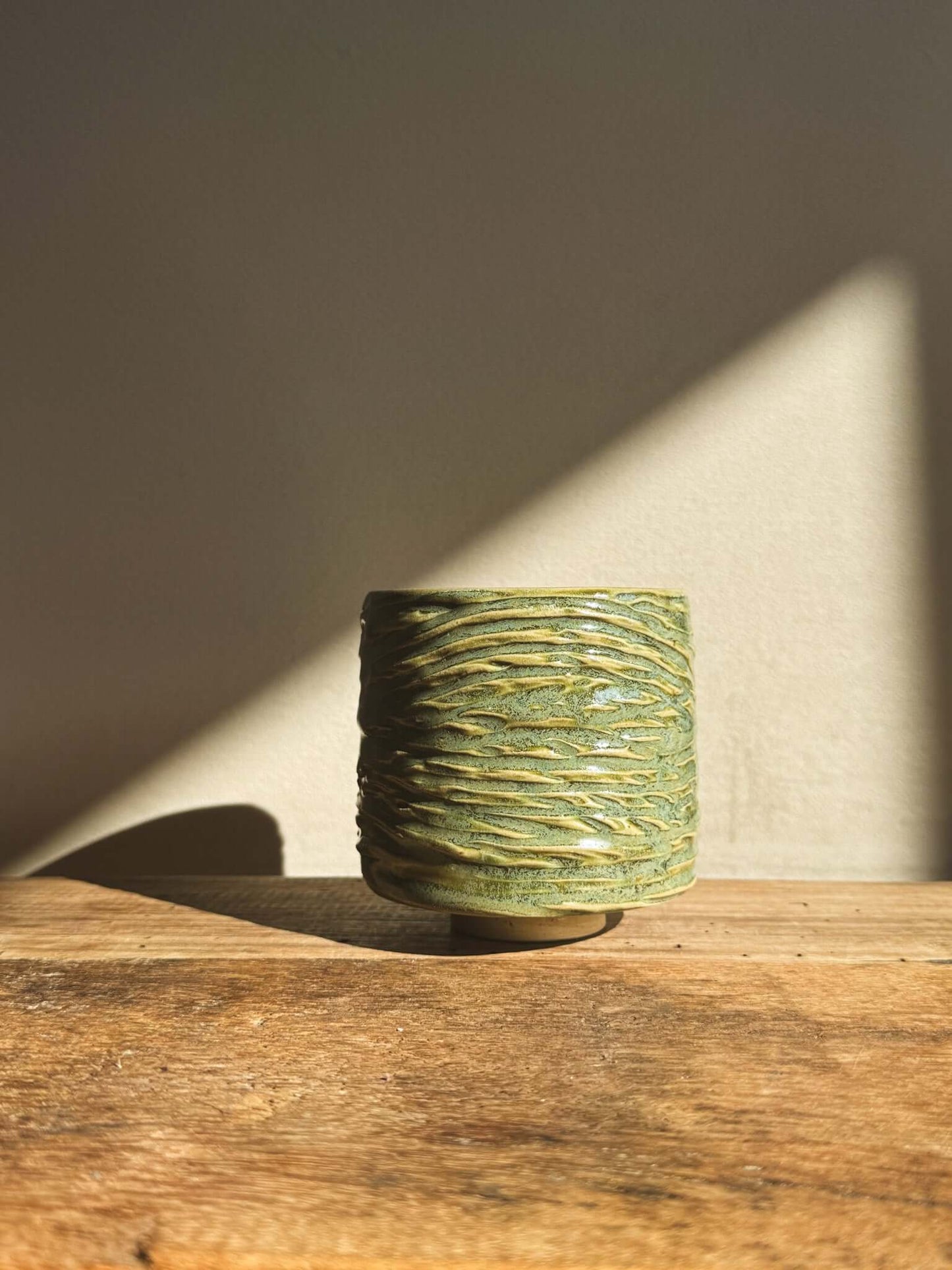 Wasabi Green Yunomi Cup with textured surface and subtle shine, displayed on wooden table with soft lighting.