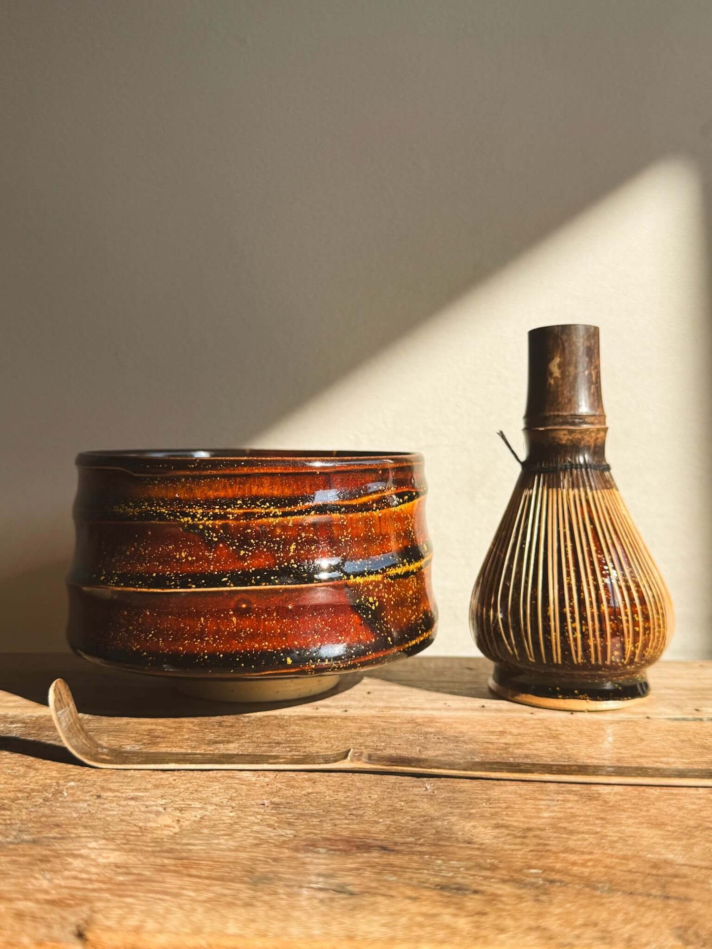 Kinsei Matcha Bowl #04 with rich amber glaze, reflecting light alongside a bamboo whisk on a wooden surface.