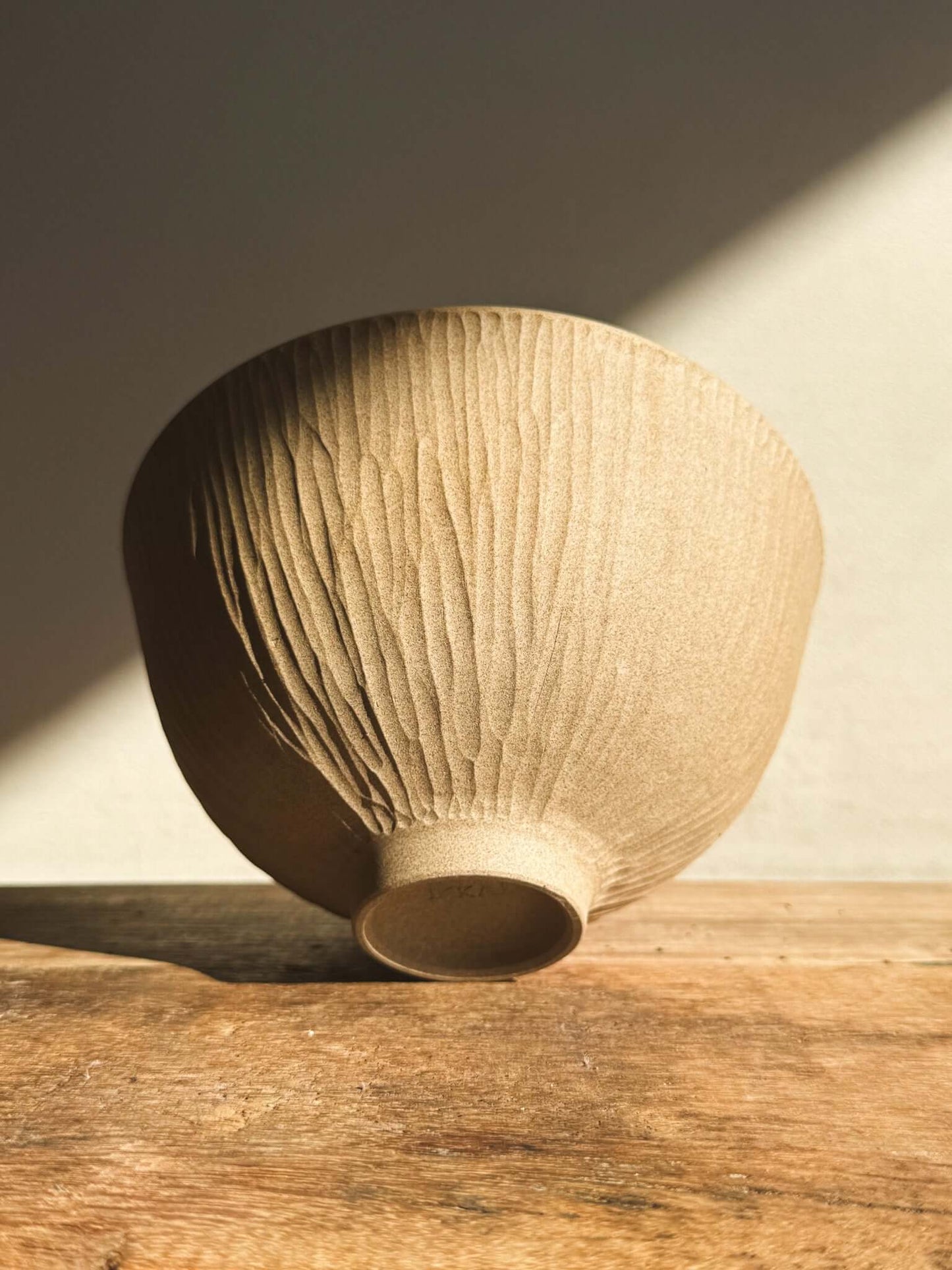 Textured Matcha bowl from Inyo Series with vertical carvings, showcasing natural clay under warm light on a wooden surface.