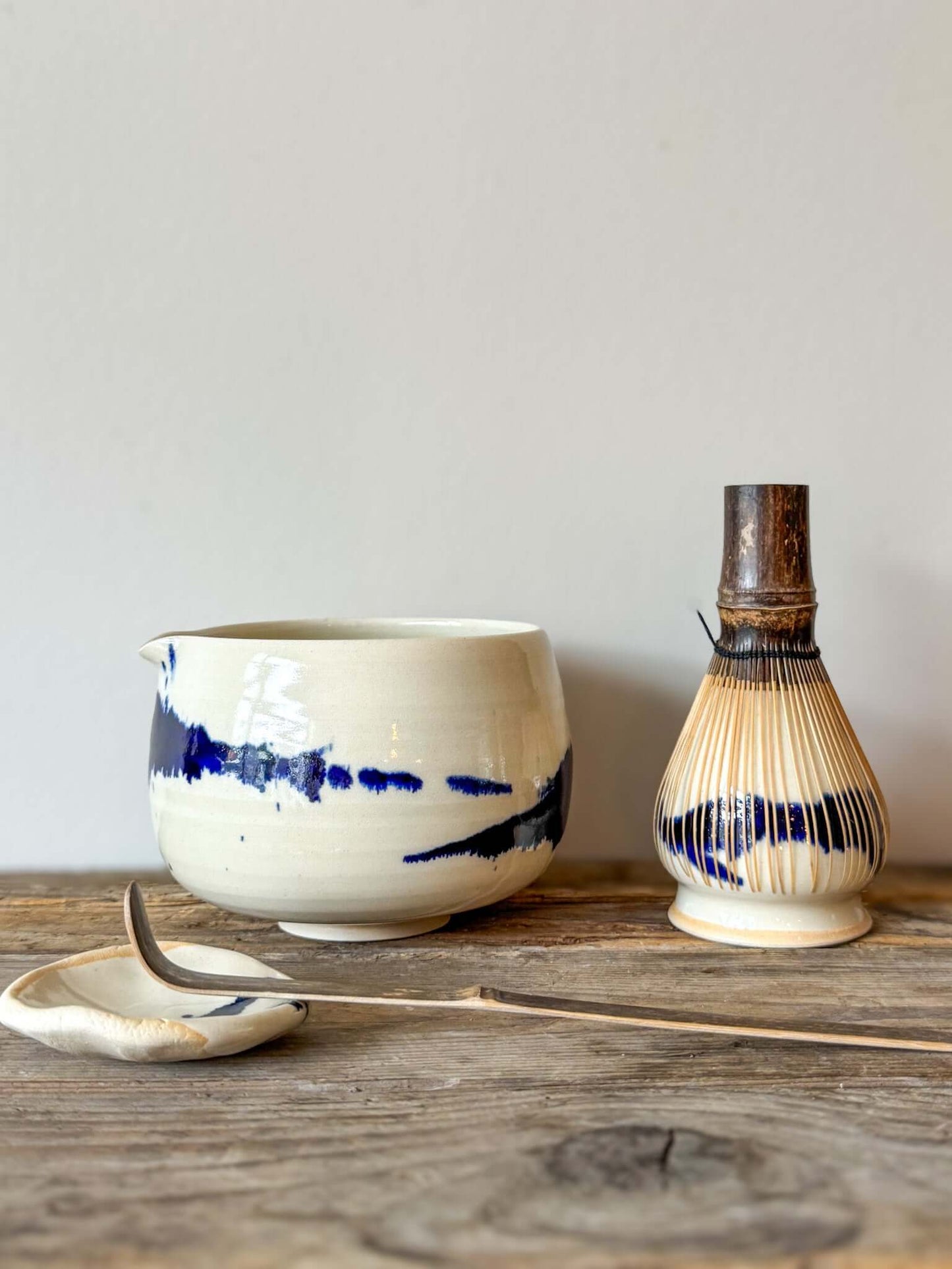 Gosu Series Katakuchi Matcha Bowl with spout, featuring dynamic cobalt blue glaze patterns, displayed with a bamboo whisk on wooden surface.