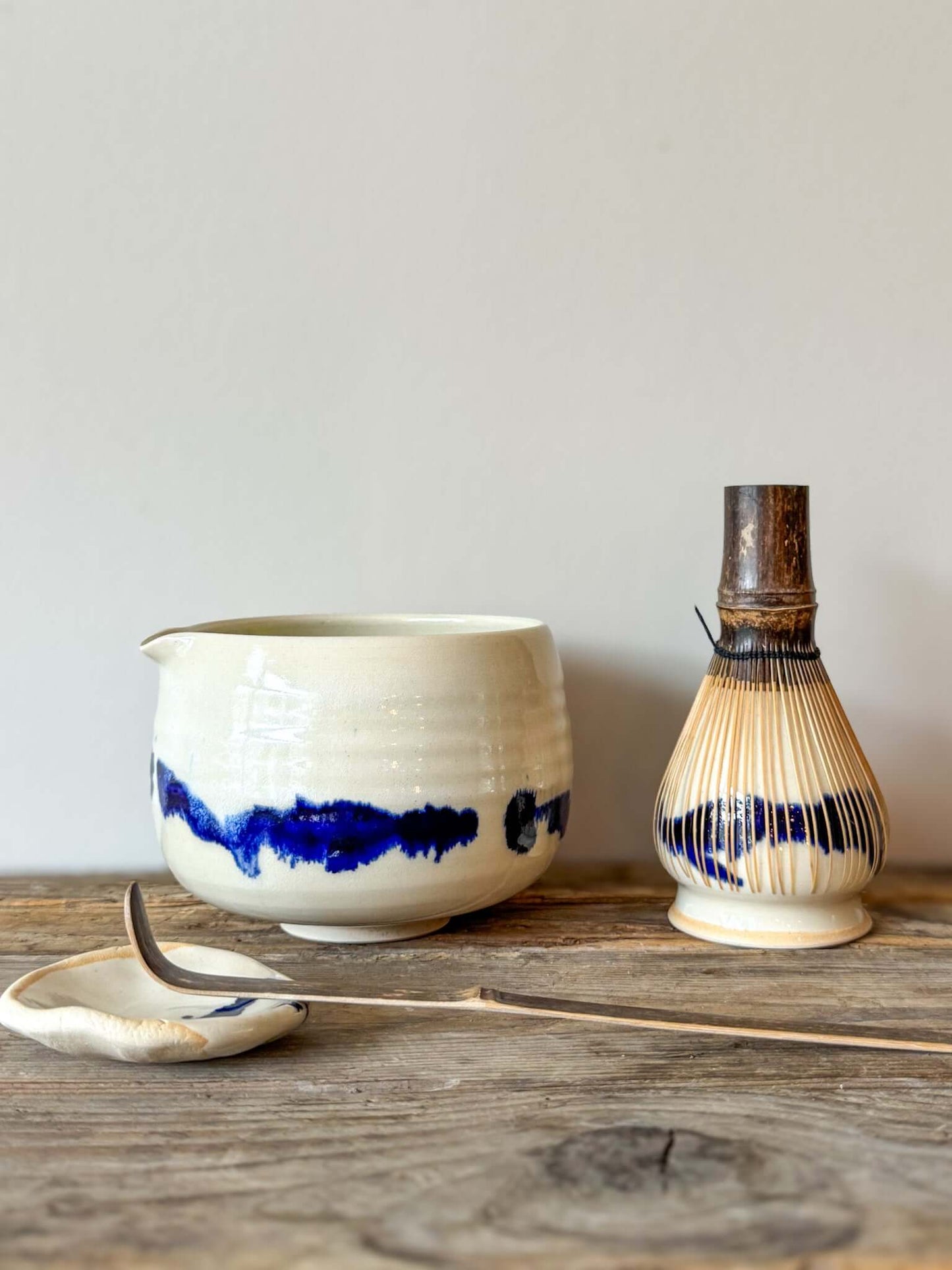 Katakuchi Matcha Bowl with Spout from Gosu Series, featuring cobalt blue glaze patterns, whisk, and spoon on a rustic surface.