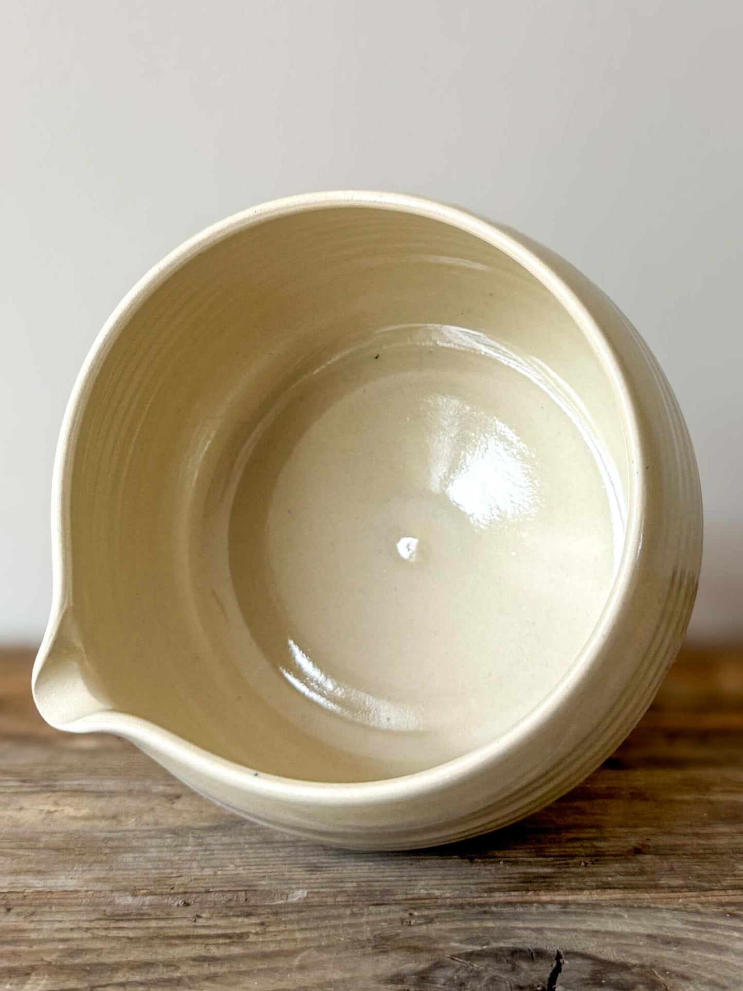 Top view of a beige katakuchi matcha bowl with a spout, displaying its smooth interior, resting on a wooden surface.