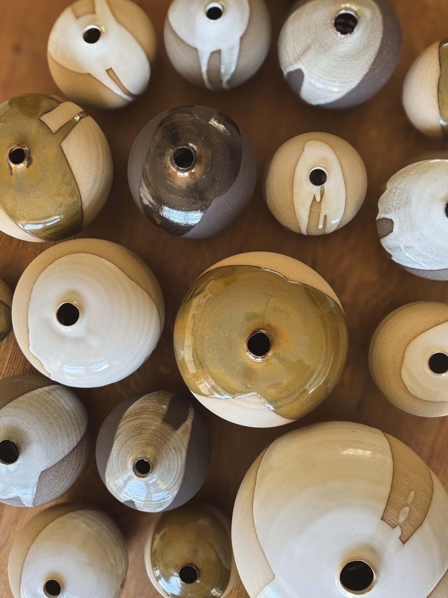 Collection of Orb Vase – #01 with varied glaze patterns and rounded shapes on a wooden surface.