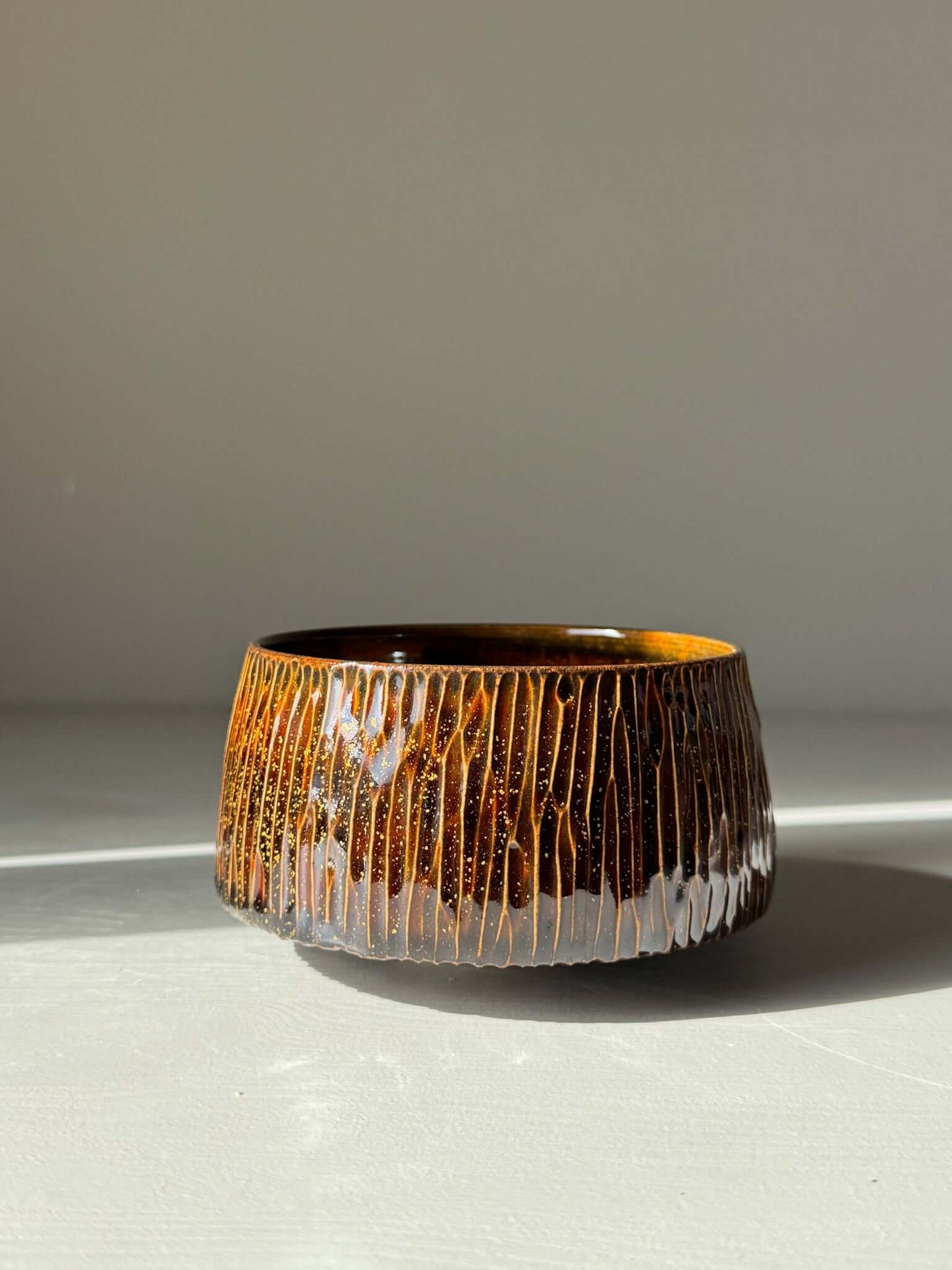 Matcha Bowl – Kinsei #03, handmade ceramic with a glossy brown exterior and gold spiral interior, glowing like a galaxy inside.