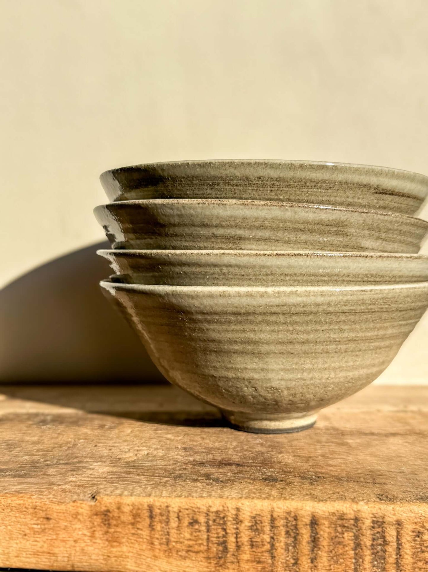 Stacked Yuki Series dark clay bowls with soft white glaze, showcasing unique wheel lines and texture, on a wooden surface.