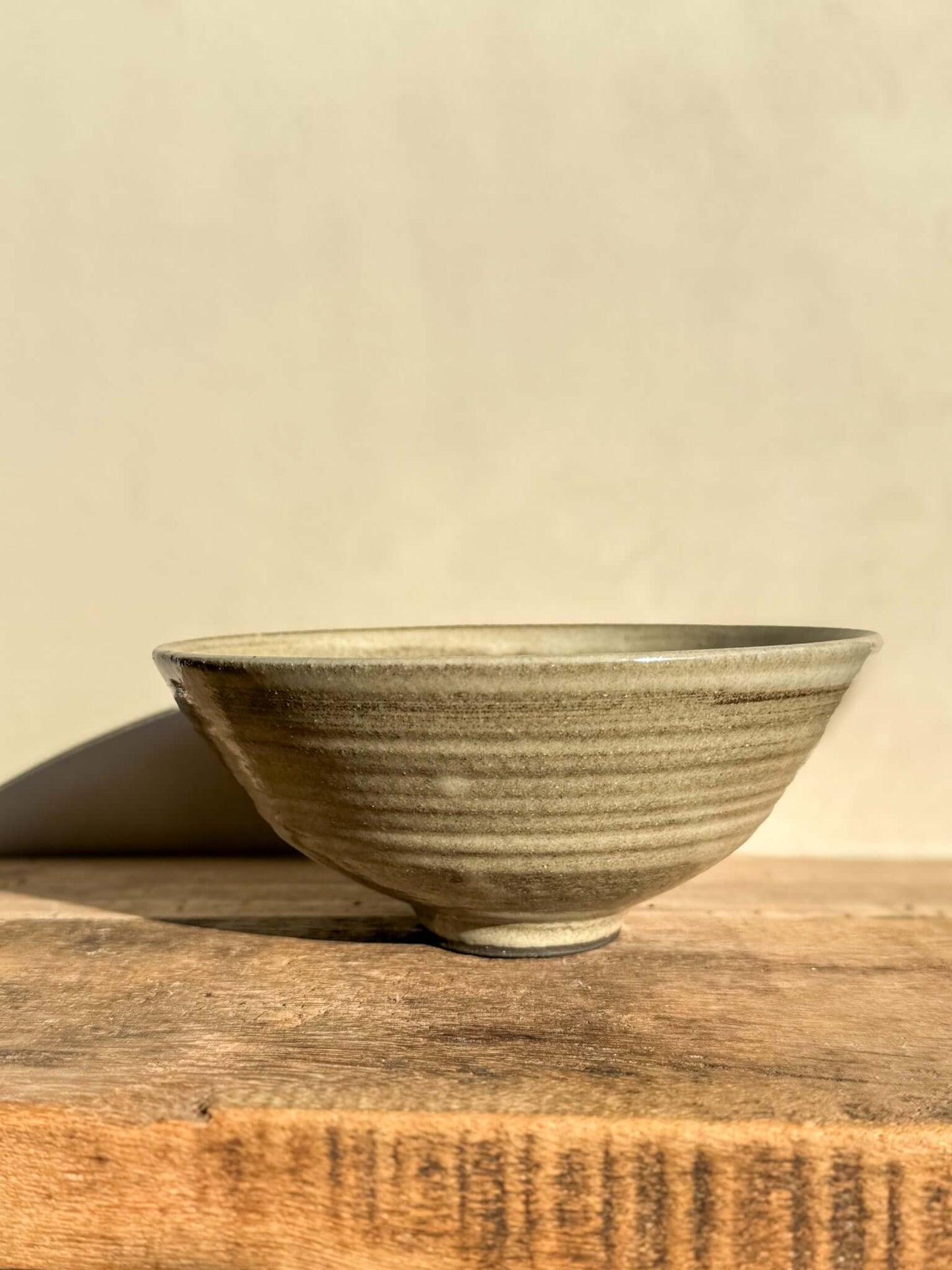 Wide Yuki Series dark clay bowl with soft white glaze on wooden surface, highlighting wheel-thrown lines and unique glaze texture.