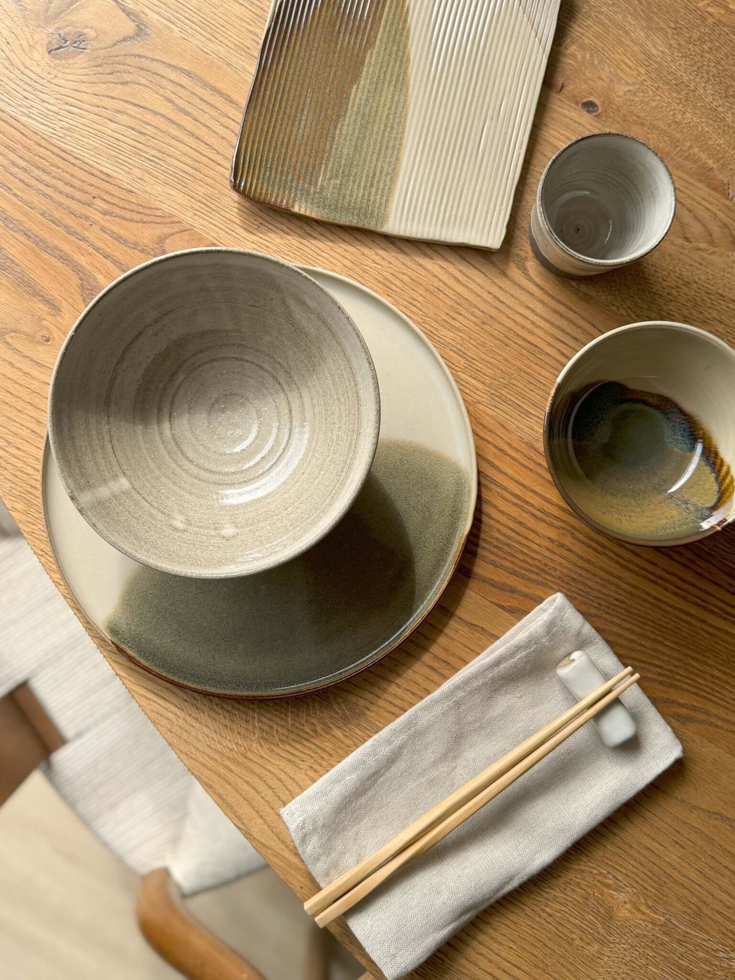 Yuki Series Dark Clay bowl with white glaze on a wooden table, surrounded by ceramic dishes and chopsticks.