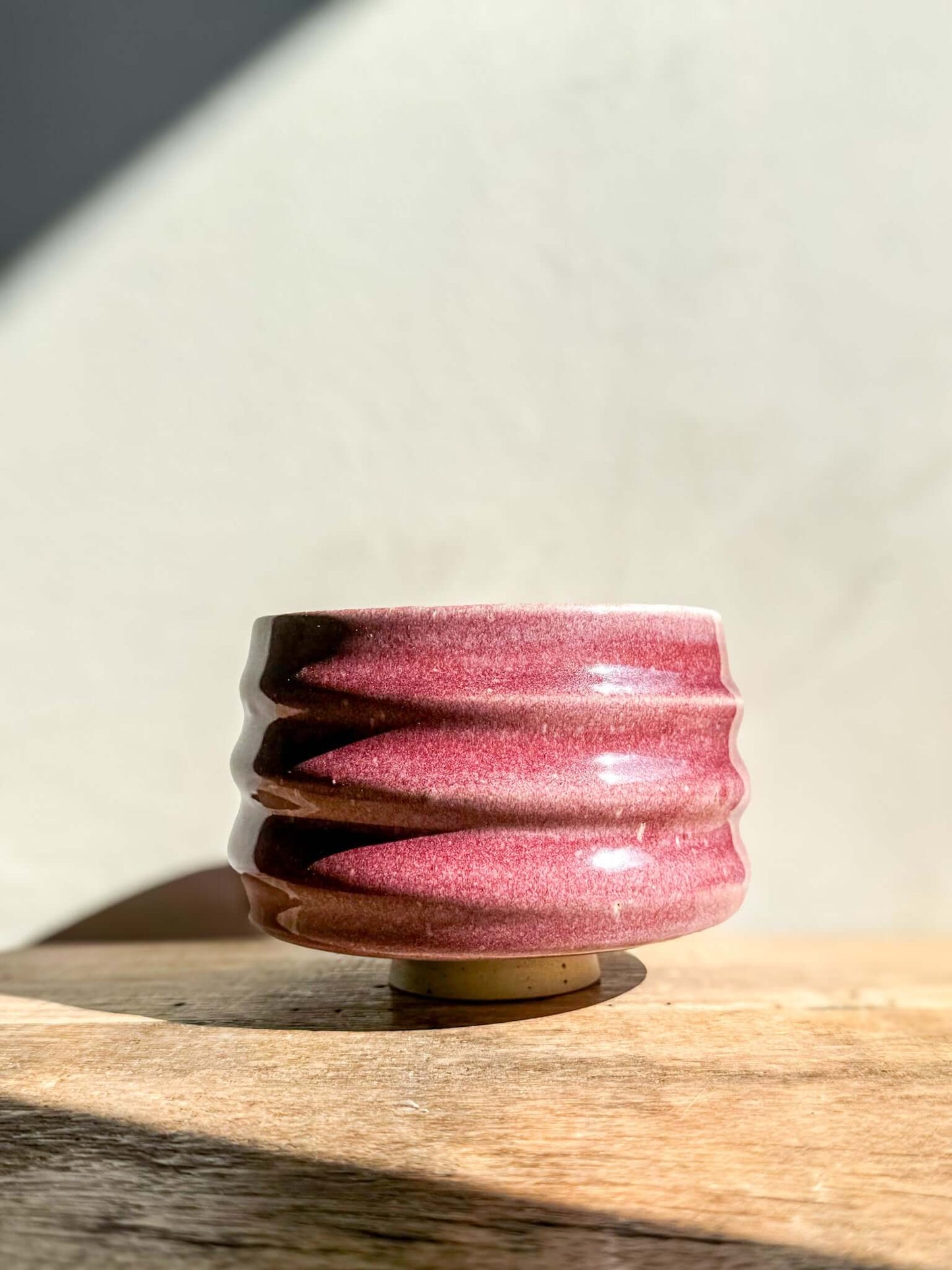 Ume Series Matcha Bowl with pink flowing ridges, inspired by Japanese blossom, symbolizing resilience and renewal on a wooden surface.