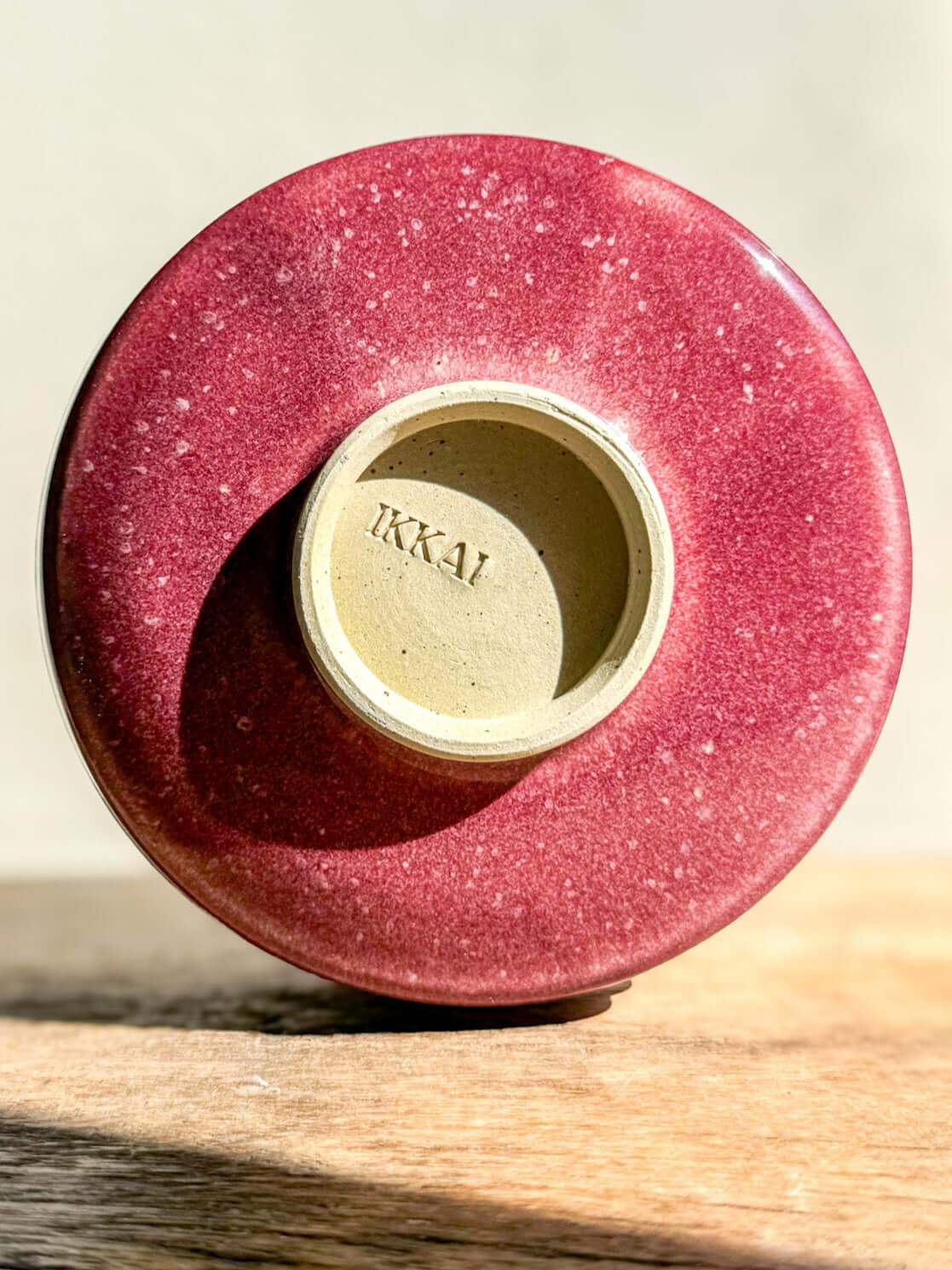 Ume Series Matcha Bowl bottom view showing the Ikkai stamp, featuring a rich red glaze with subtle speckles on a wooden surface.