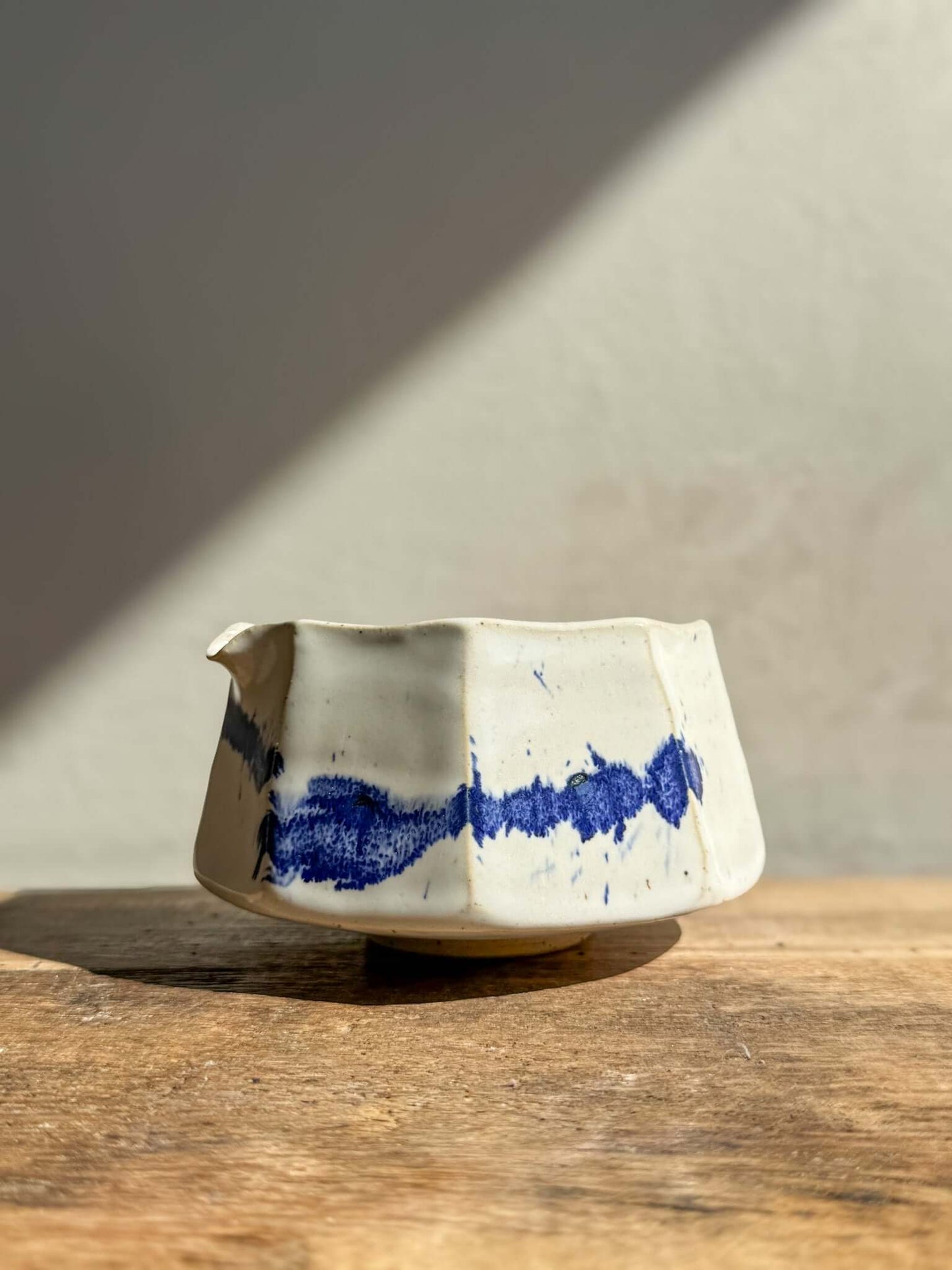 Faceted matcha bowl with spout in cobalt blue and glossy white glaze, hand-crafted with a modern design and textured facets.