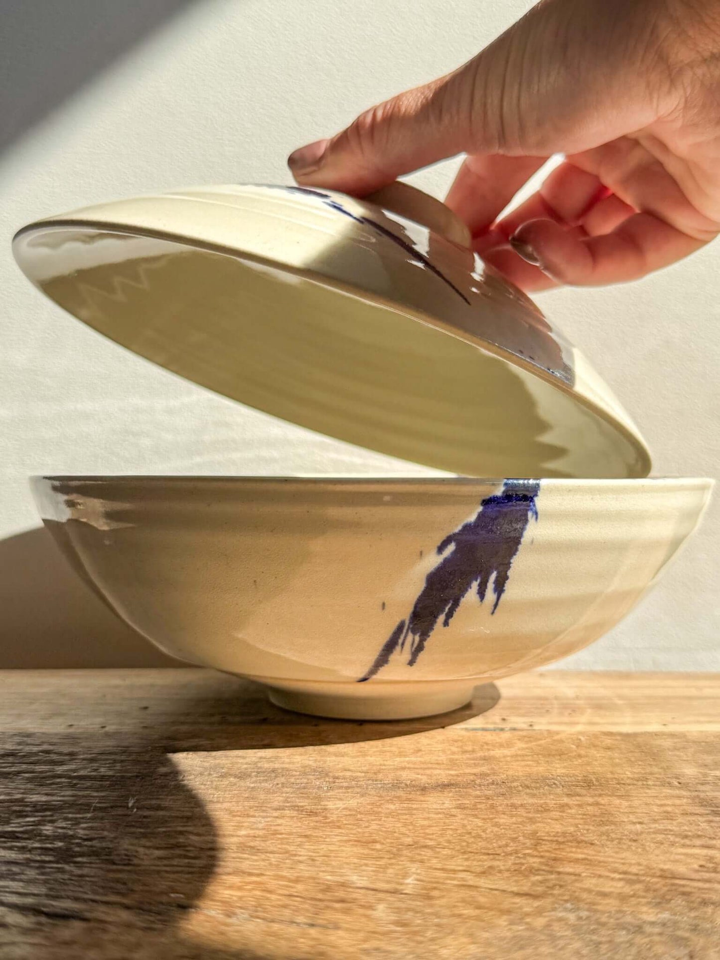 Lidded Serving Bowl from the Gosu Series with bold cobalt splashes, handcrafted design being revealed.