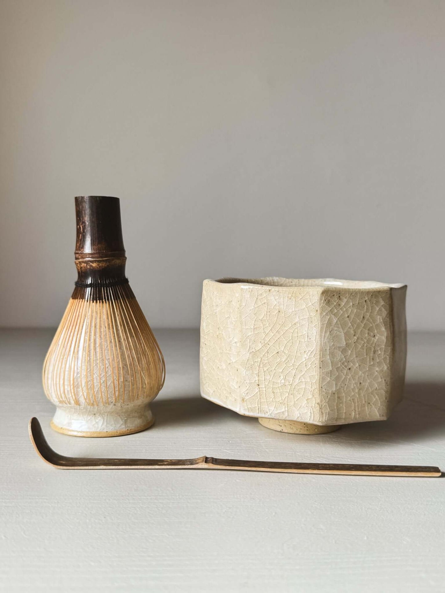 Faceted matcha bowl with honey-toned crackle glaze, alongside a bamboo whisk and traditional chashaku spoon.