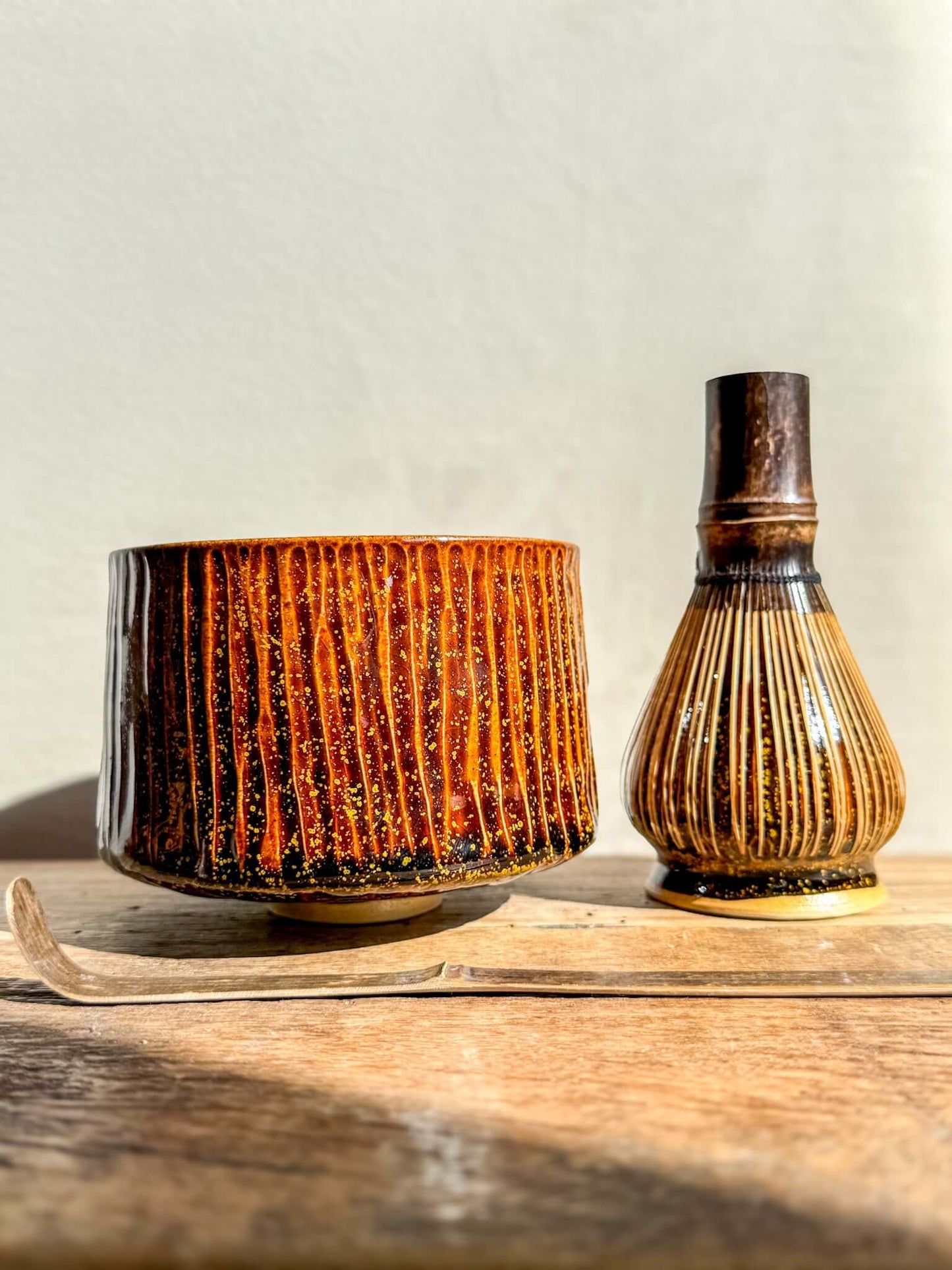 Kinsei Matcha Bowl #02 with rich brown glaze and gold spiral, paired with a traditional whisk, displayed on wooden surface.