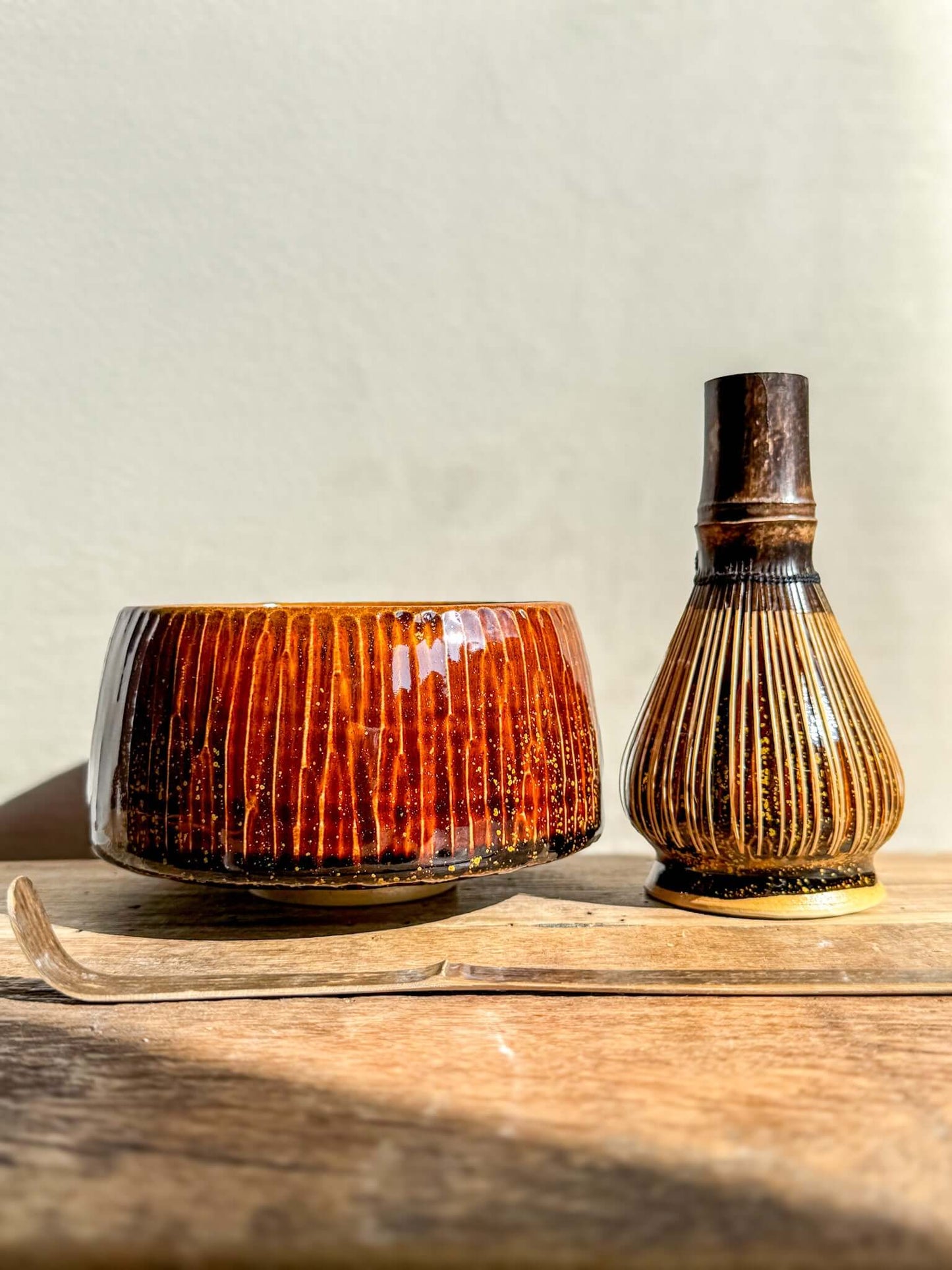 Kinsei #03 matcha bowl with bamboo whisk, glossy brown exterior, gold spiral inside, displayed on a wooden surface.