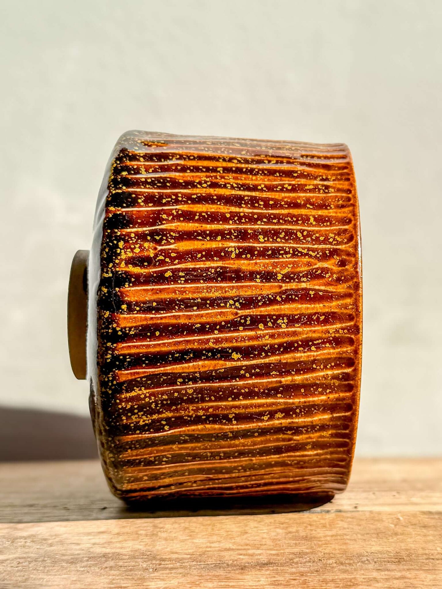 Side view of Kinsei #02 Matcha Bowl with rich, glossy brown glaze and carved texture, resembling a galaxy with golden star accents.