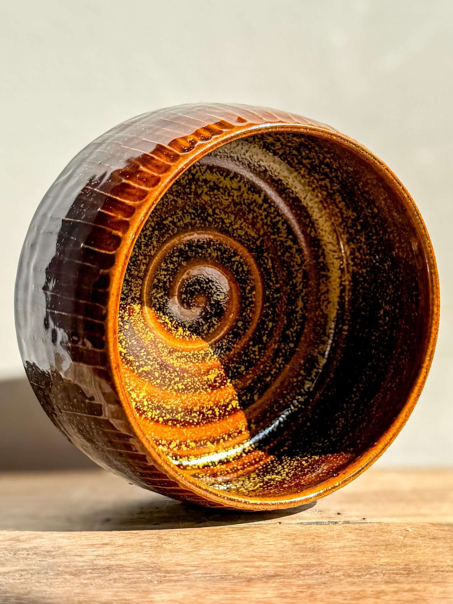 Kinsei #03 matcha bowl with glossy brown exterior and gold-orange spiral interior, resembling a radiant galaxy captured in clay.