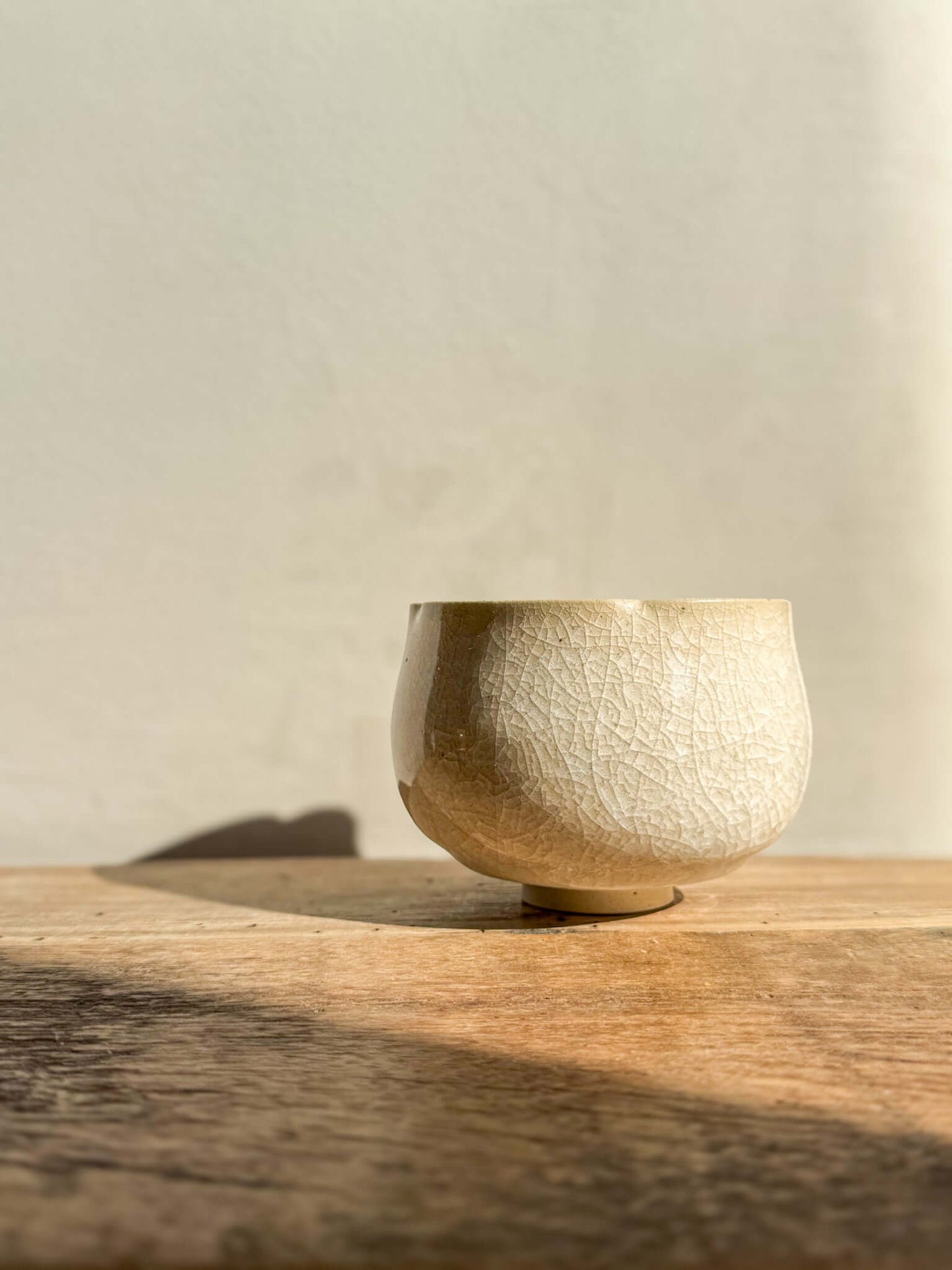 Yunomi Cup from Kannyū Series with crackle glaze, resting on a wooden surface, showcasing elegant fine lines and soft rim design.