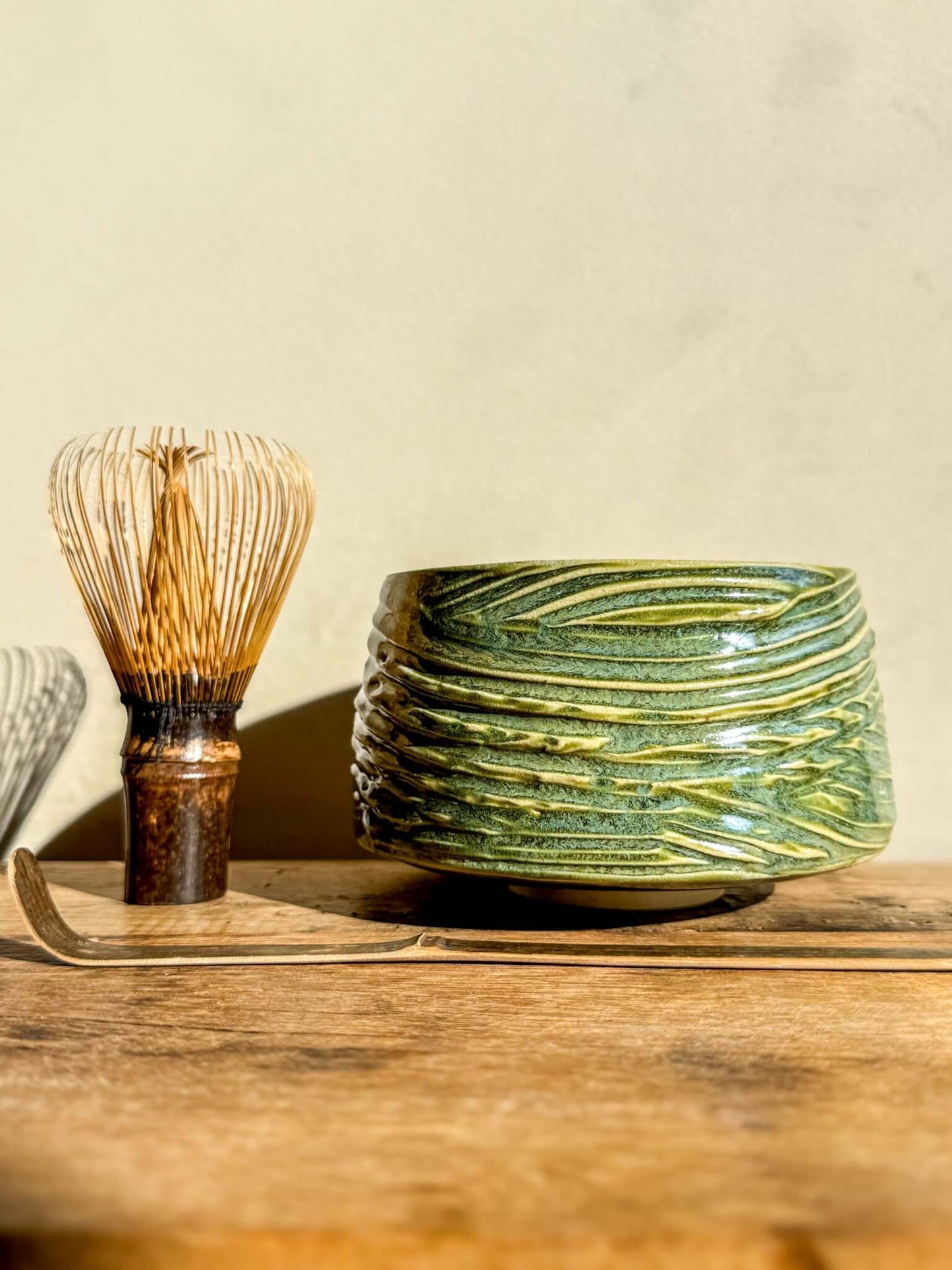 Wasabi green matcha bowl with textured surface and bamboo whisk on wooden table, showcasing unique glaze and organic lines.