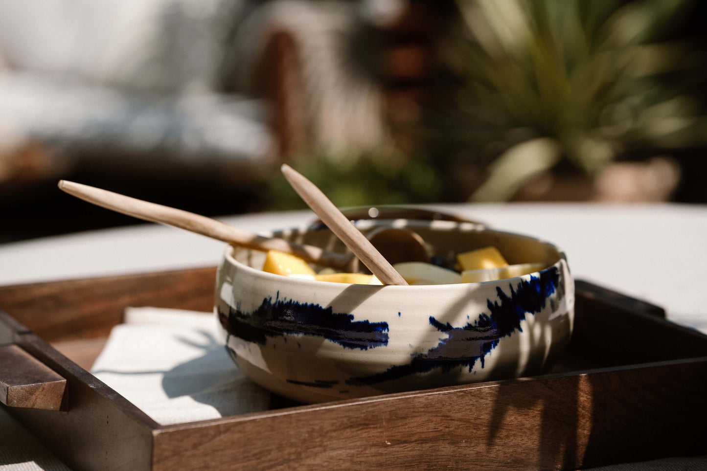 Hand-carved walnut wood serving spoon in a ceramic bowl with fruit on a wooden tray outdoors, highlighting artisan craftsmanship.