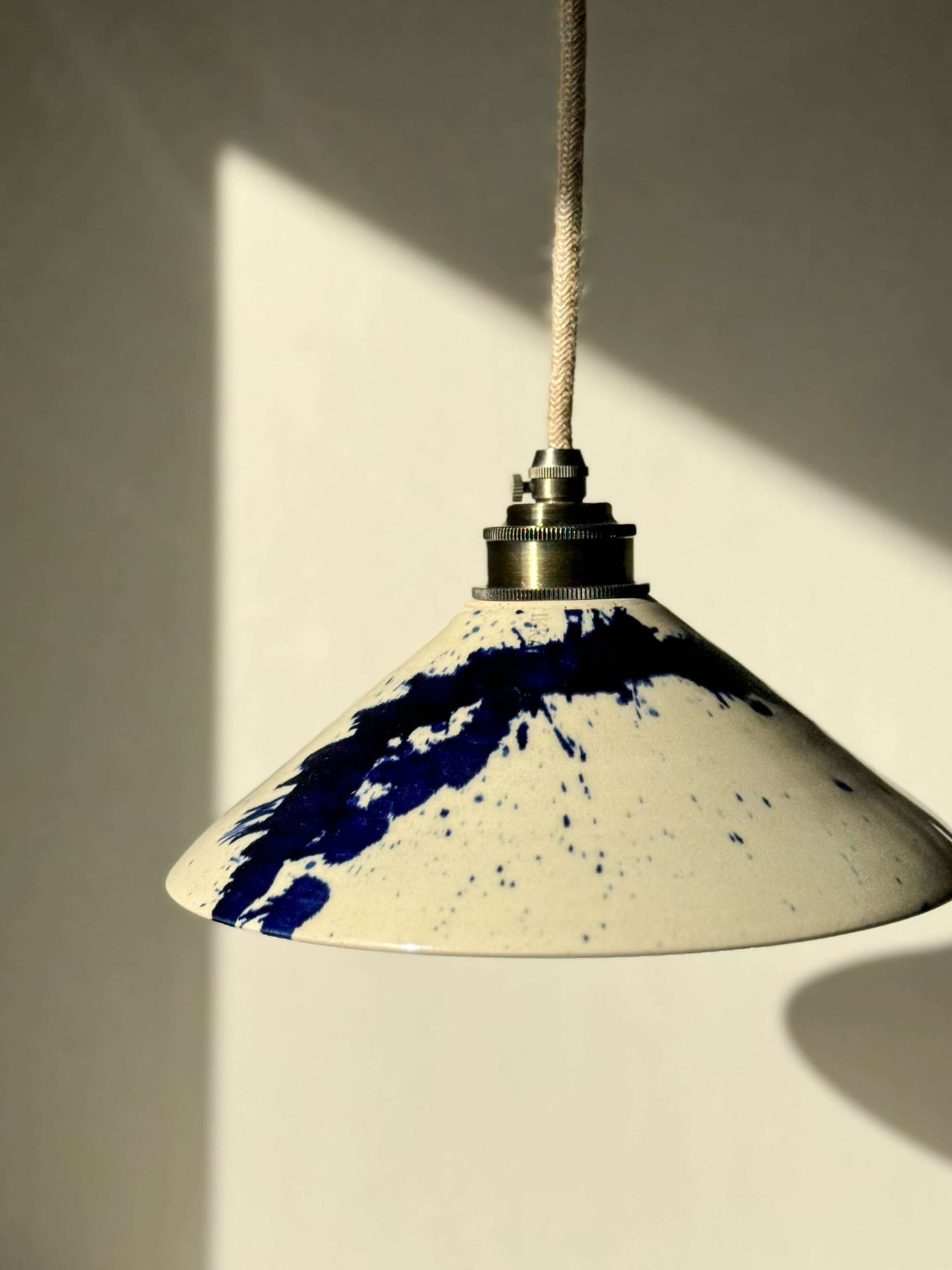 Handmade ceramic lamp shade from Gosu Series with cobalt blue accents, featuring a glossy finish, hanging in sunlight.
