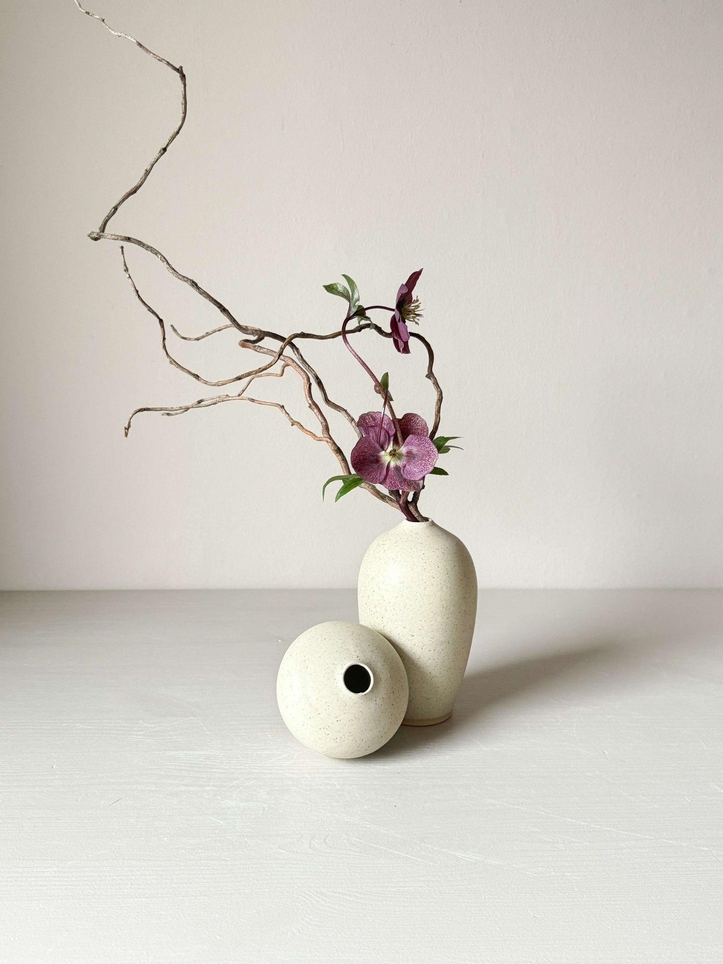 Ceramic vase with speckled matte cream glaze, arranged with delicate flowers and branches, showcasing elegant and timeless design.