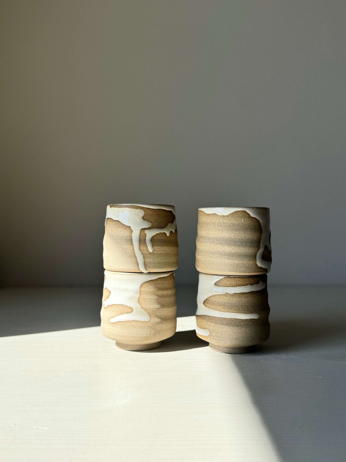 Pair of handmade Yuki Series espresso cups with flowing white glaze and toffee-toned clay, showcasing natural warmth and subtle design.
