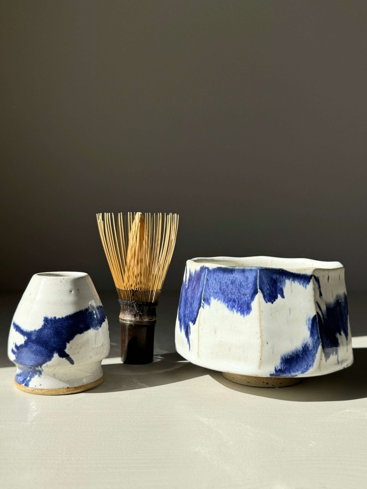 Faceted matcha bowl with cobalt blue accents and bamboo whisk set on a white surface.