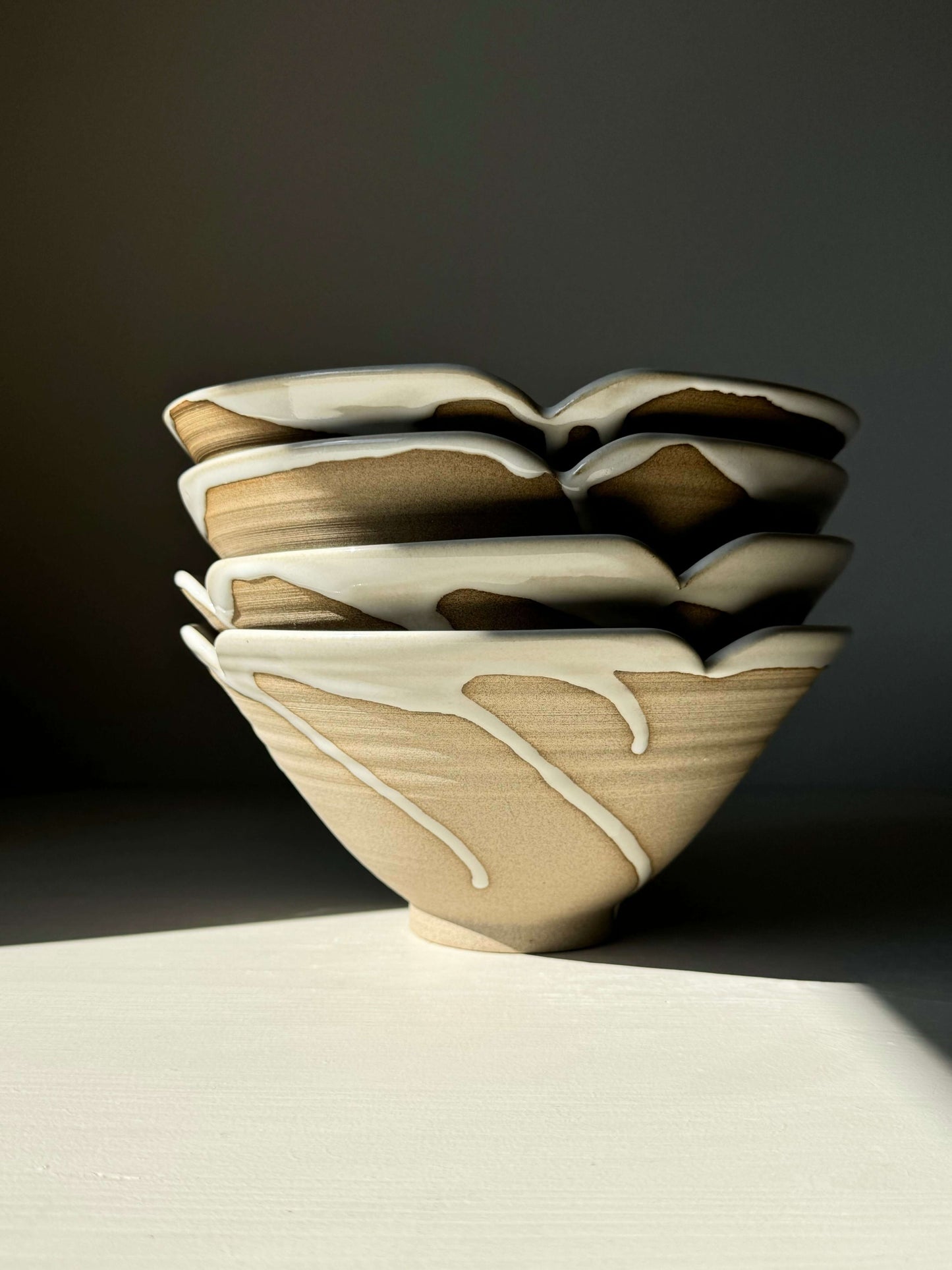 Stack of handmade ceramic bowls with glossy dripped glaze on a dark background, showcasing artistic craftsmanship and natural elegance.