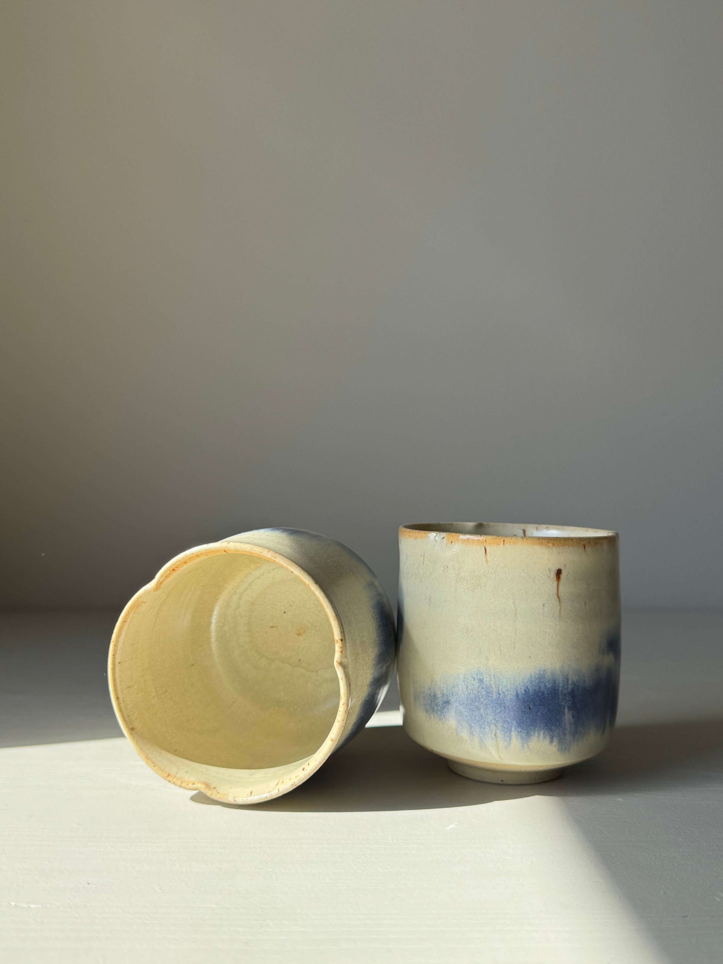 Cobalt blue and moonstone glaze yunomi cups with flower-shaped rims, featuring a high-fired stoneware clay and tenmoku glaze finish.
