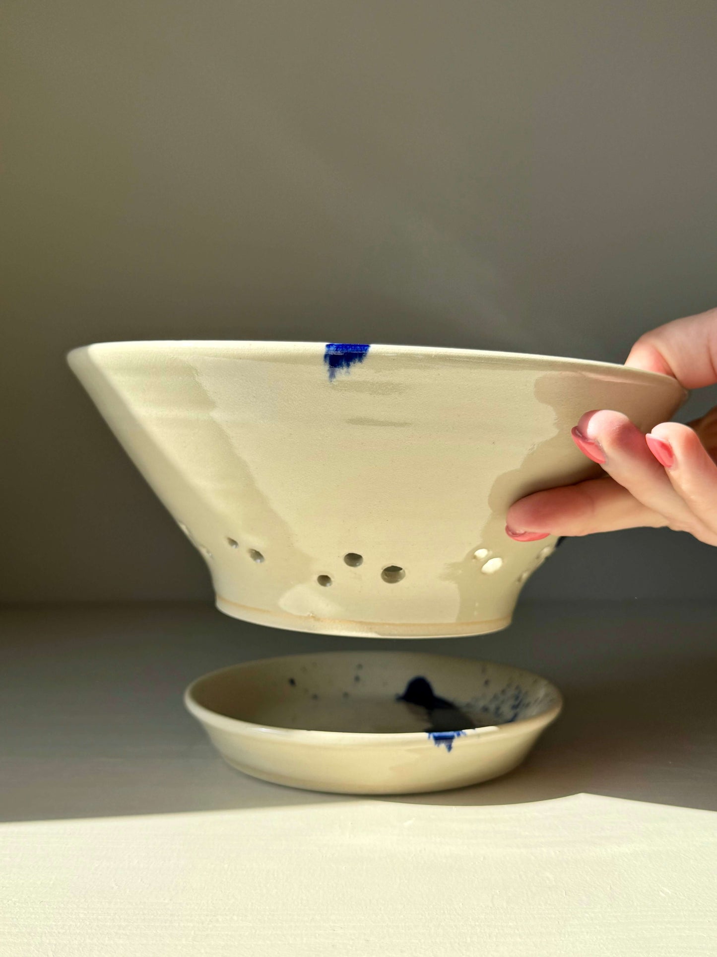 Hand holding Gosu Series sculptural berry bowl with cobalt splashes, accompanied by a matching drip plate. Ideal for fresh fruit.