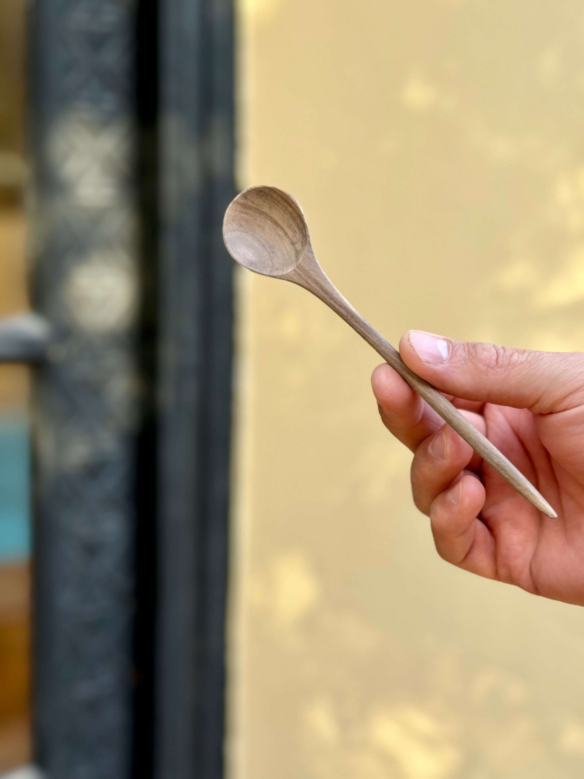 Hand holding a Hand-Carved Walnut Tea Spoon, perfect for stirring coffee or tea, with a handmade ceramic texture.