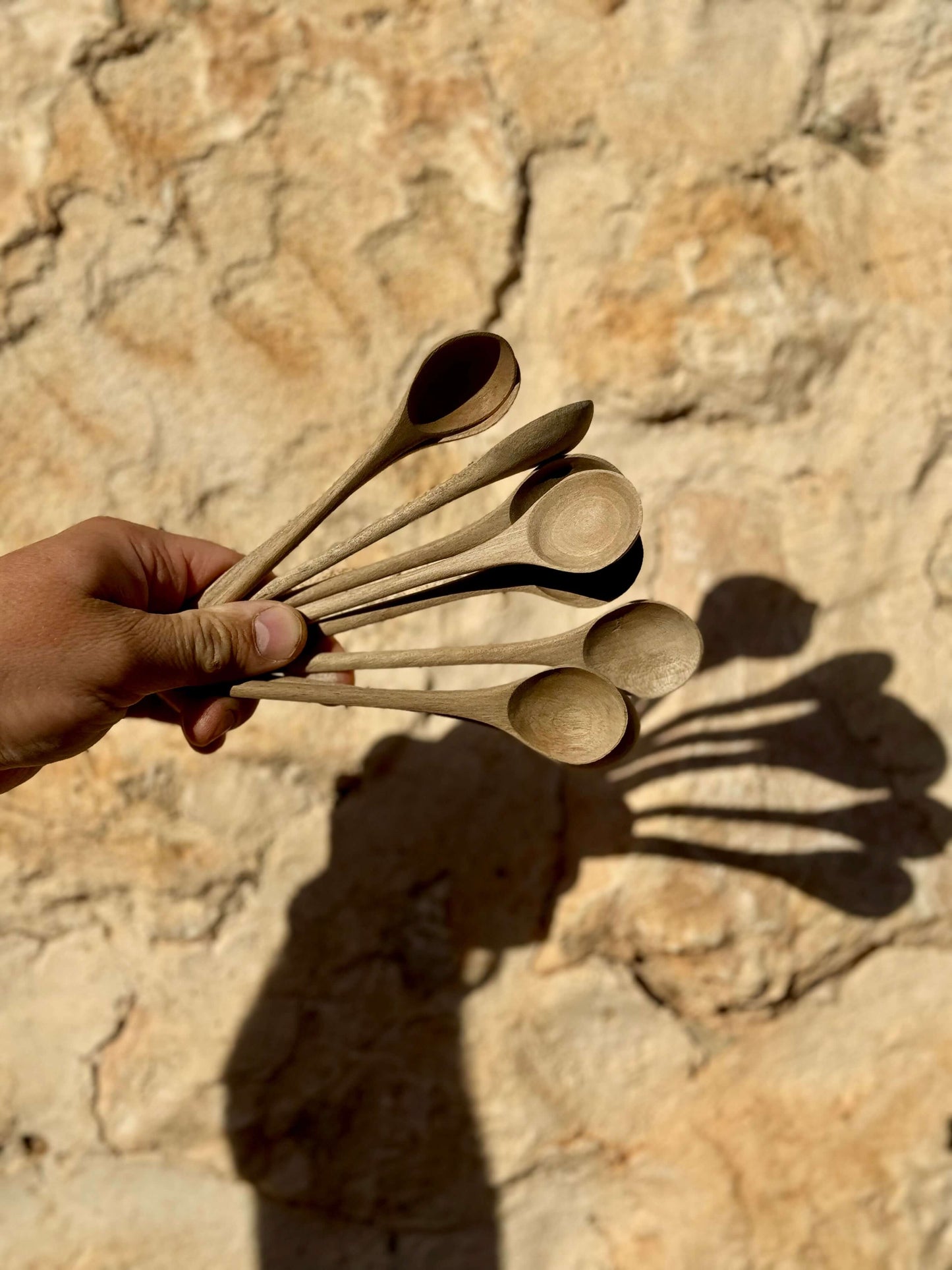 Hand holding a set of hand-carved walnut tea spoons against a textured stone background, showcasing craftsmanship and natural wood charm.