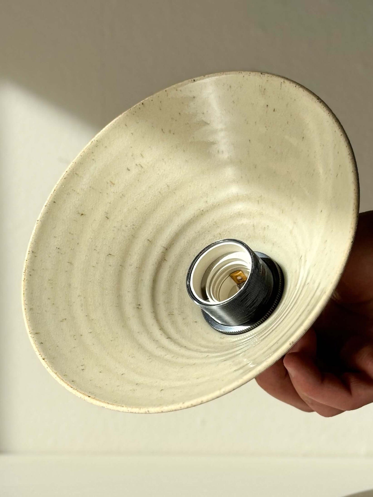 Hand-holding ceramic lamp shade with unglazed exterior and clear glazed interior, emphasizing texture and warm glow.
