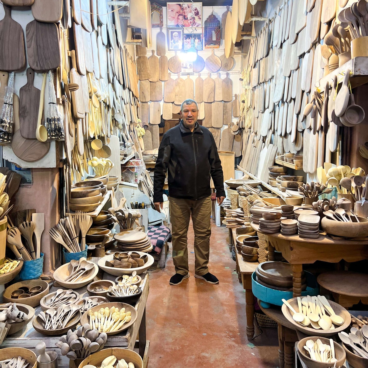 Artisan standing in a woodshop surrounded by handmade wooden utensils and serving spoons in Marrakech, showcasing local craftsmanship.