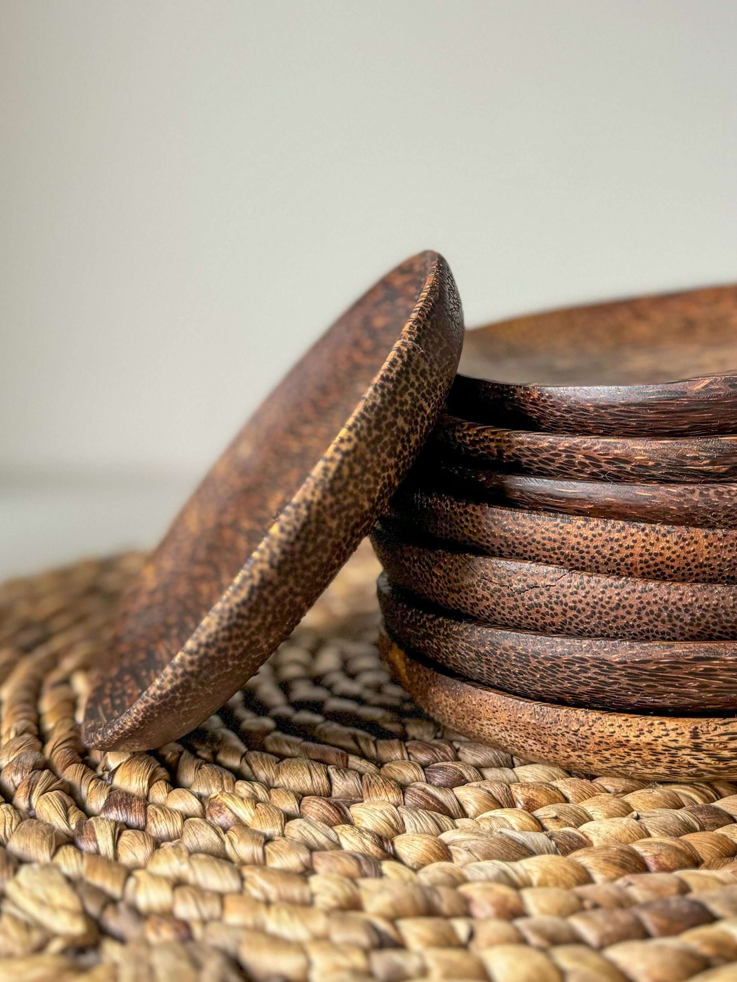 Stack of handcrafted coconut wood side plates with unique grain patterns on a woven placemat, showcasing a natural and organic look.