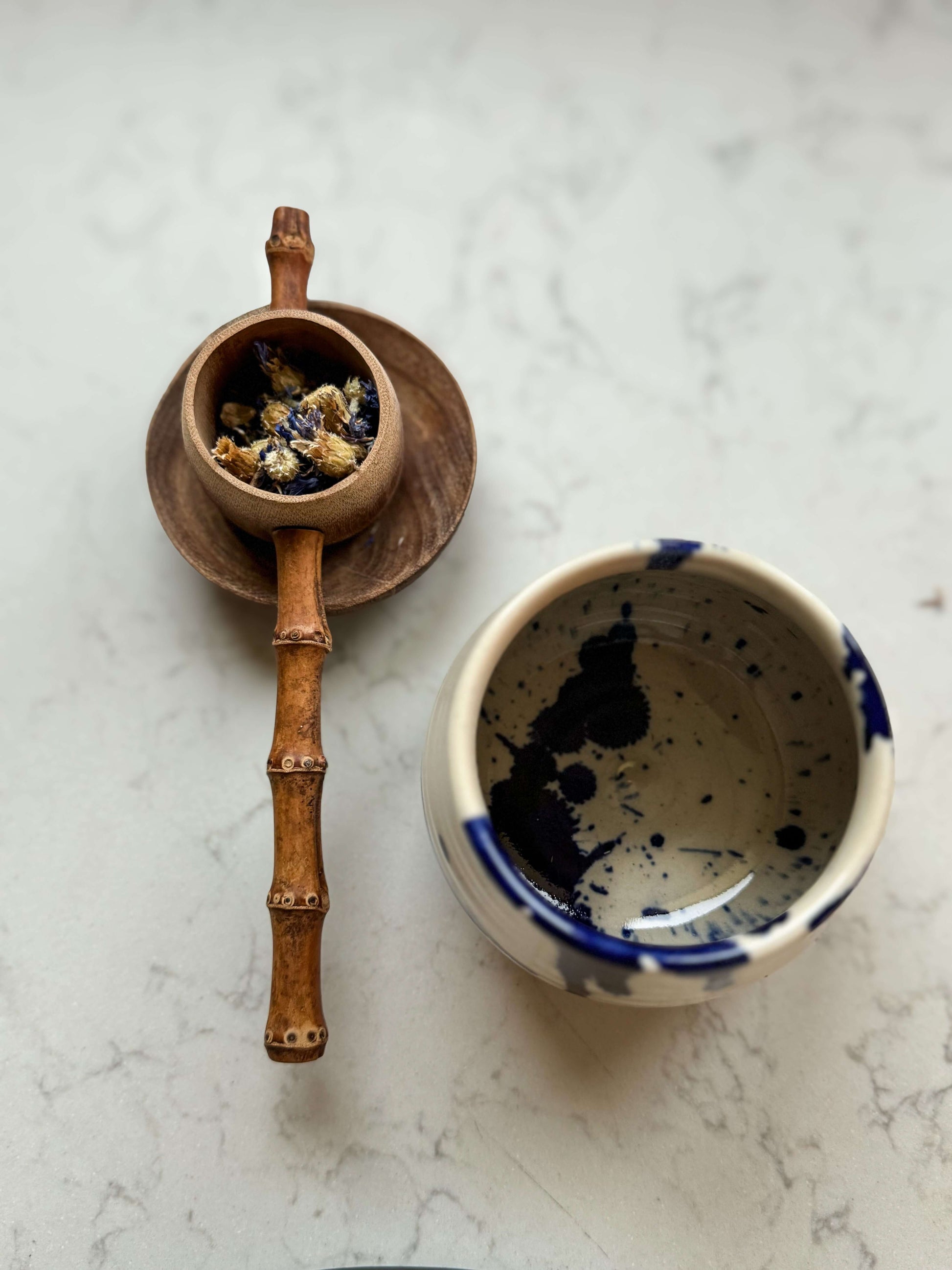 Handmade Bamboo Tea Strainer next to a handmade ceramic cup on a marble surface.