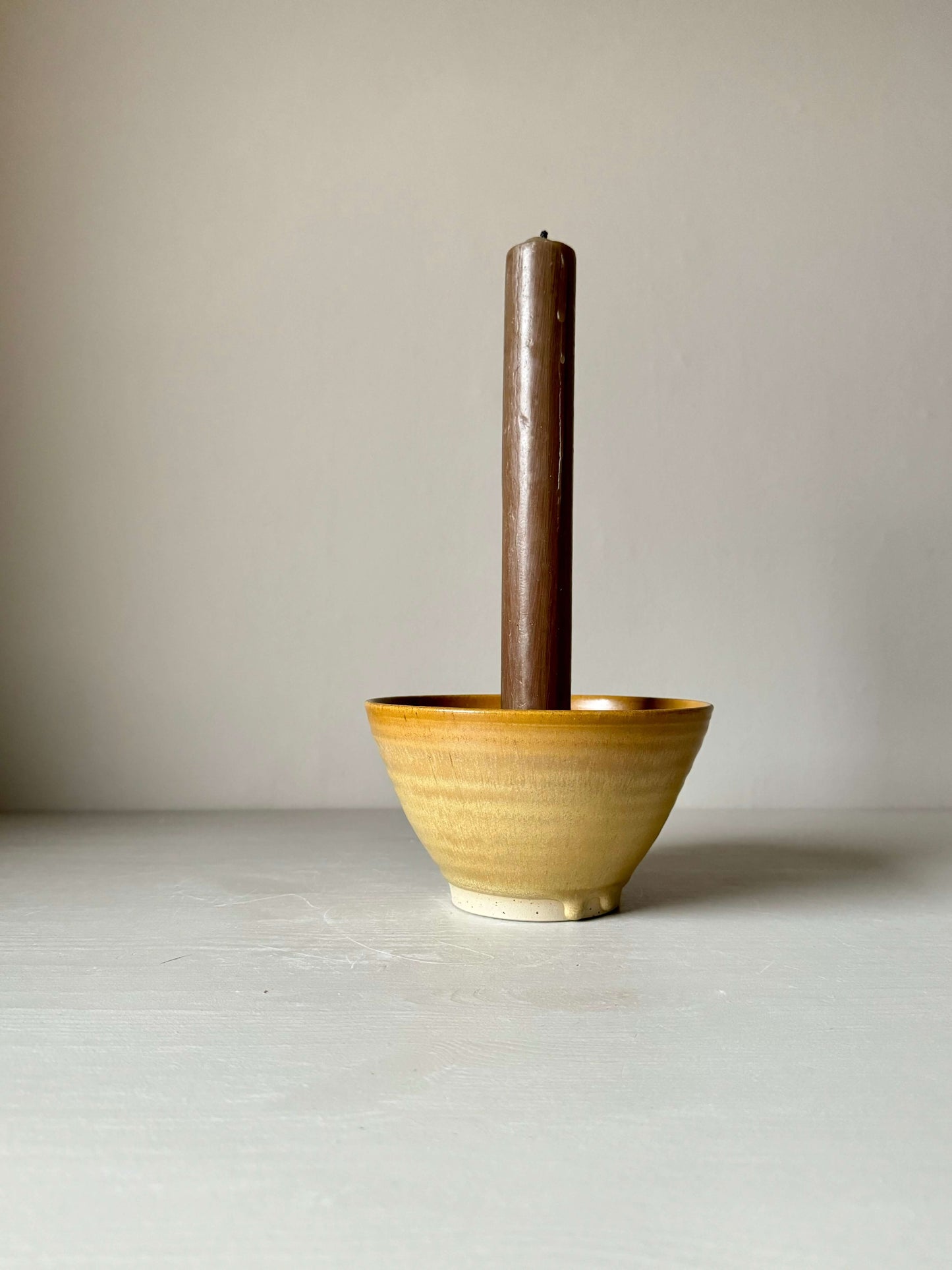 Golden Yellow stoneware candlestick holder with brown candle, handmade and wheel-thrown with unique glaze finish, placed on a light surface.