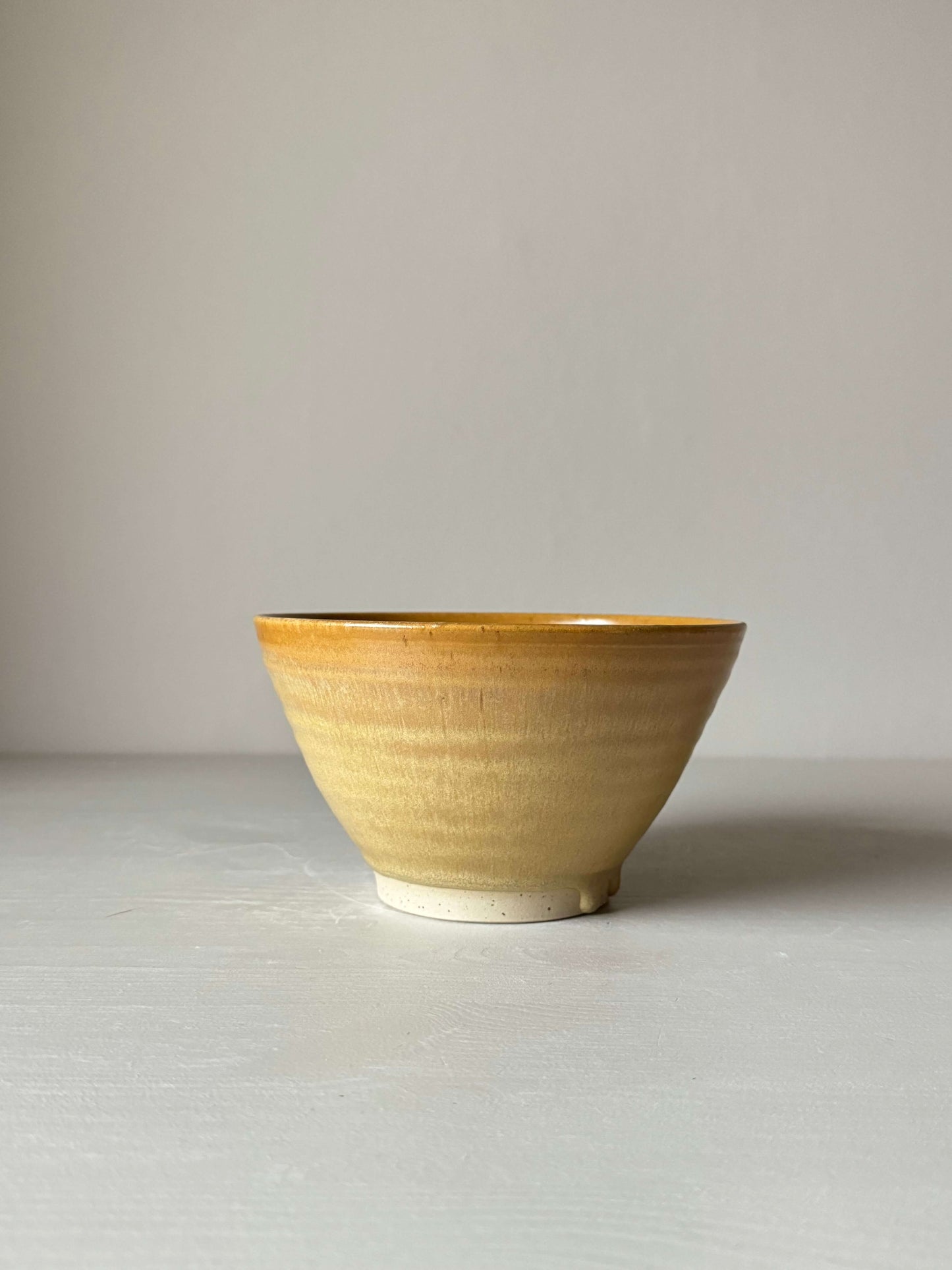 Golden yellow wheel-thrown stoneware candlestick holder, handmade with a unique glaze, 9cm tall, 15cm diameter, on a light surface.