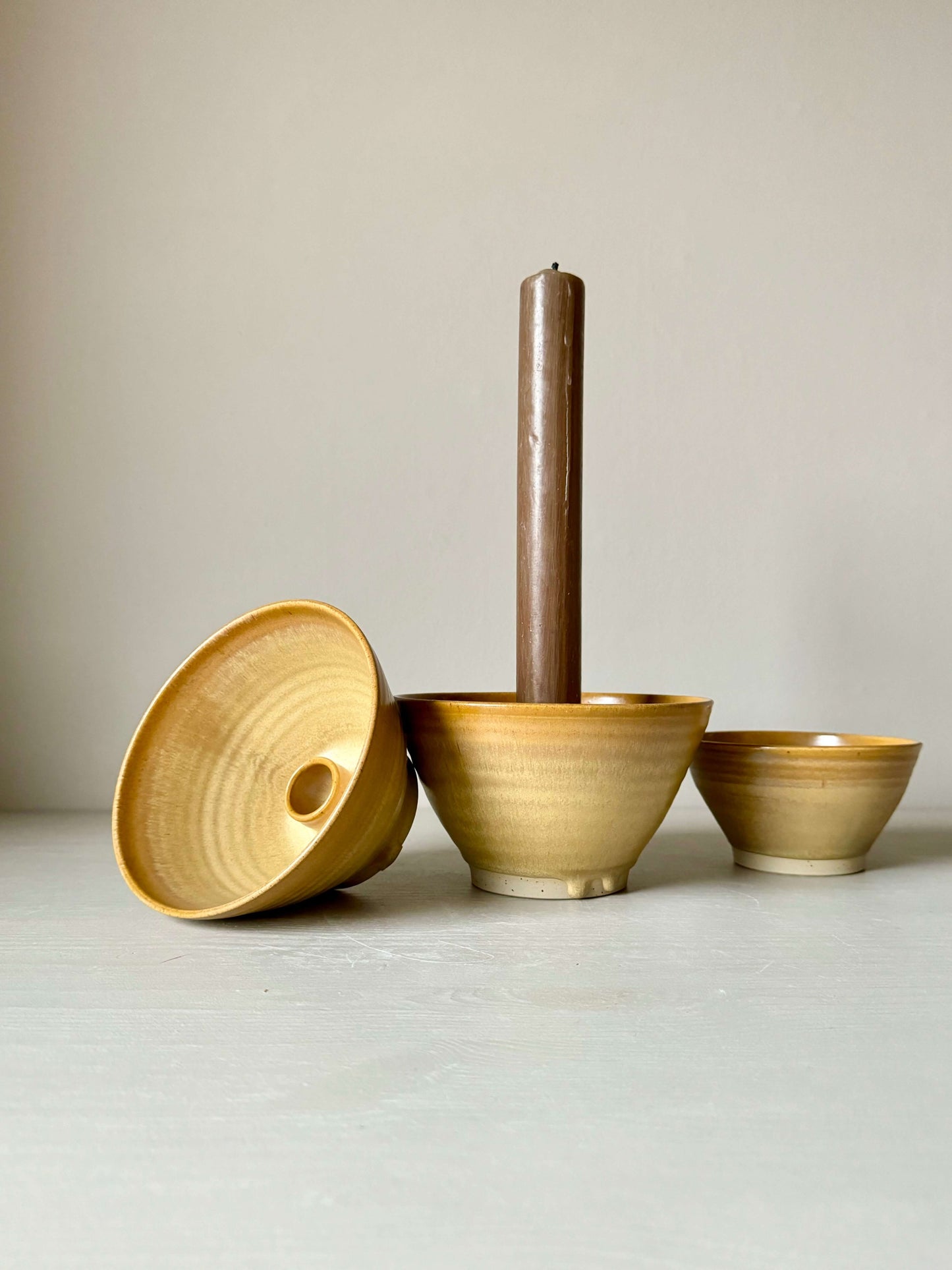 Handmade golden yellow stoneware candlestick holder set with a standing brown candle, showcasing unique craftsmanship and natural variations.
